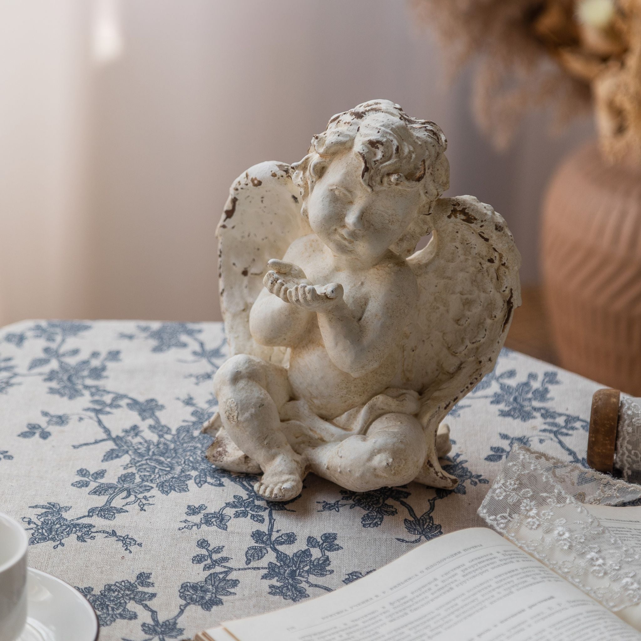 Élodie sitting cherub angel sculpture on a blue toile tablecloth, front view