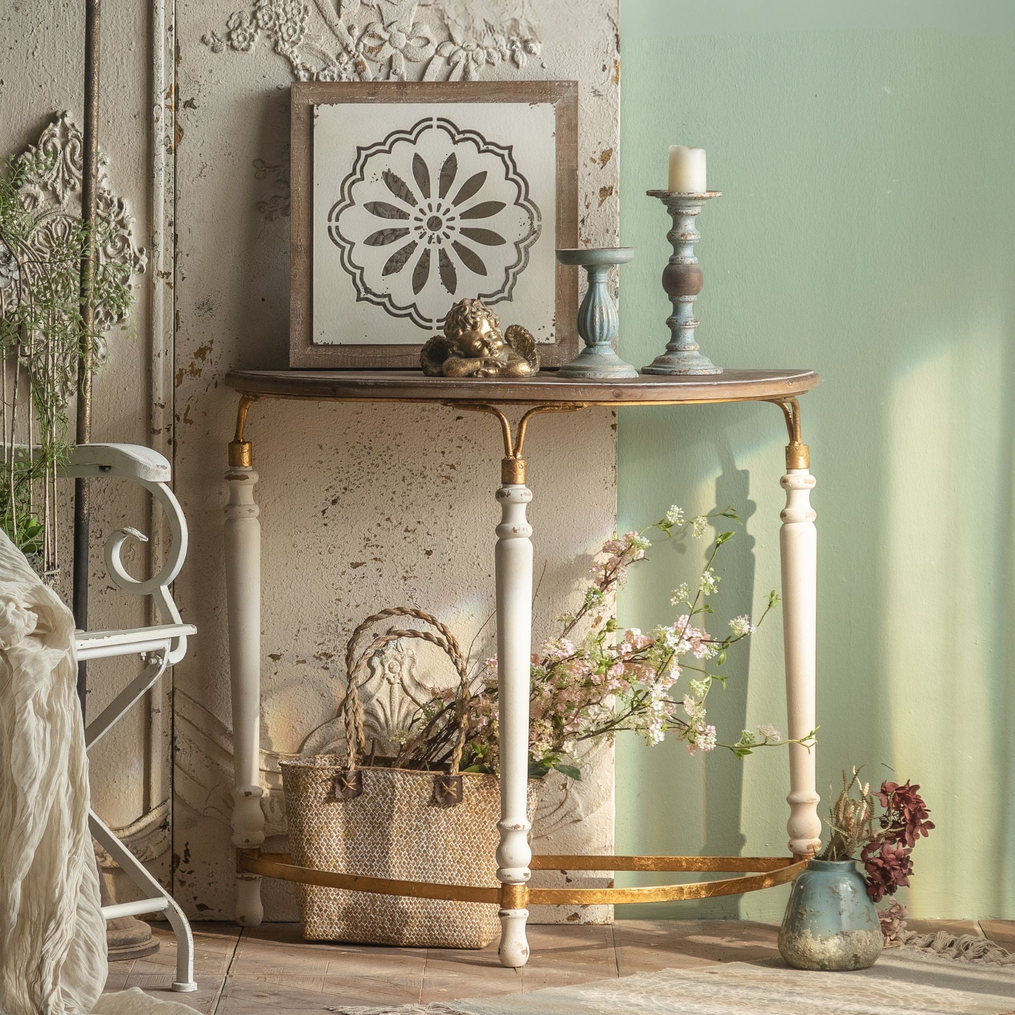 Estelle French Provincial half moon console table in distressed cream, styled in a Provençal entryway with floral stencil art, cherub and aged candlesticks. Hero.