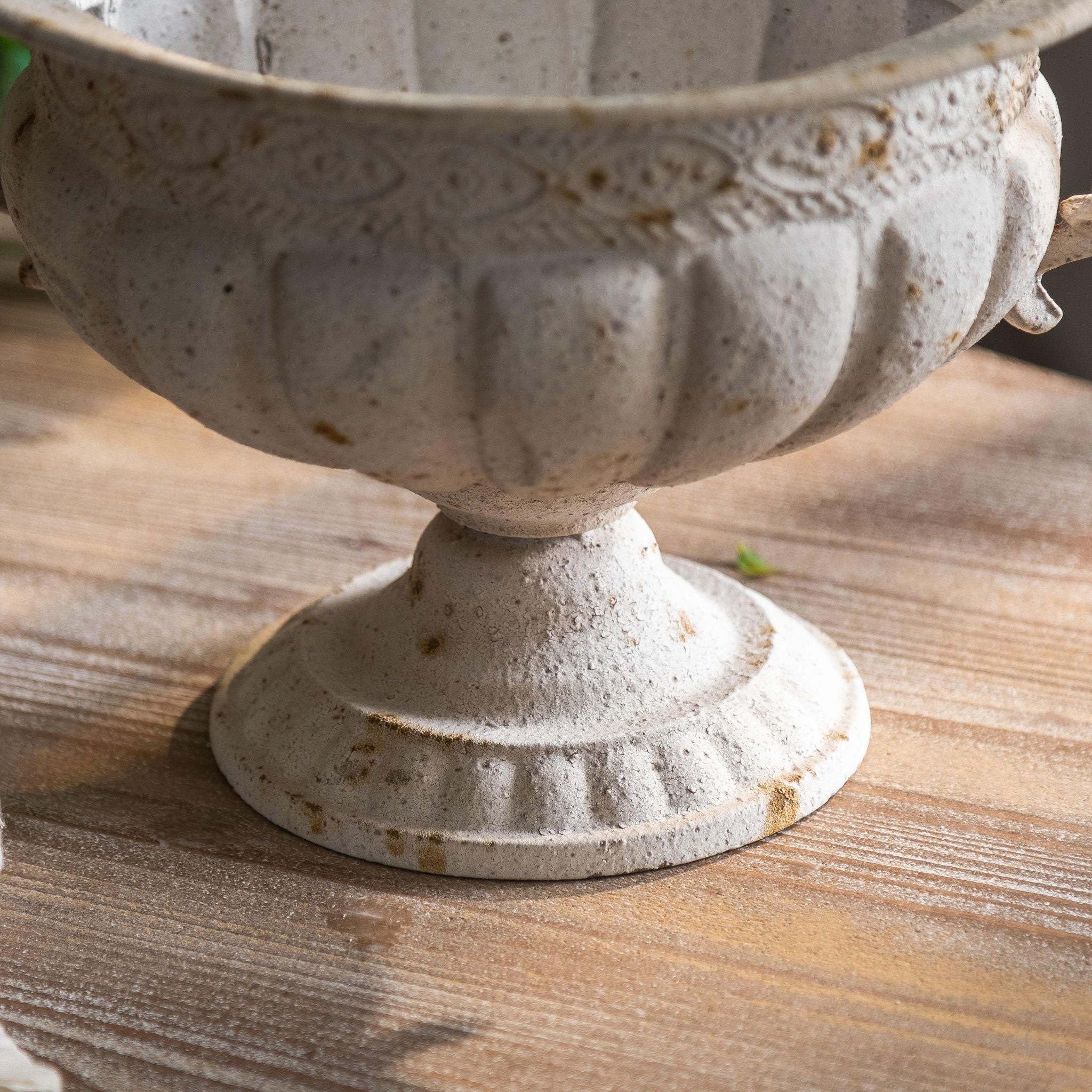 Close-up of the Fabien urn gadrooned bowl, guilloche band and pedestal foot in chalky white with rust speckle.
