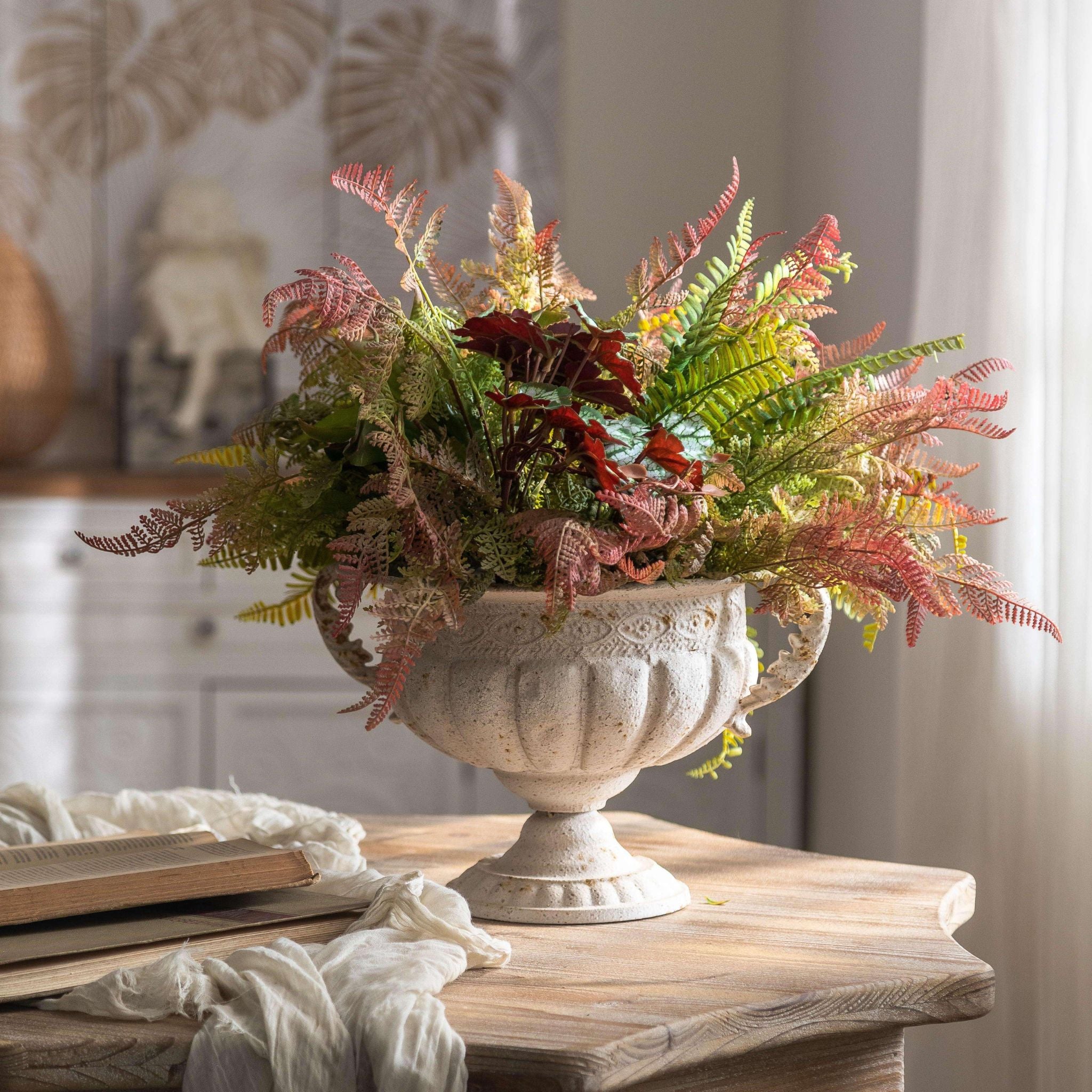 Fabien French Provincial compote urn planter in distressed antique white, planted with autumn foliage. Hero.