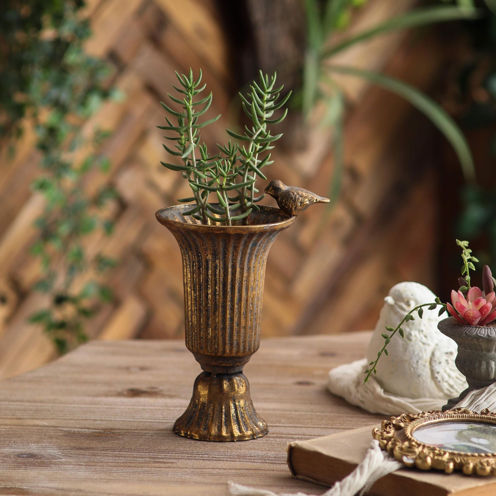 Fernande urn vase styled in a garden setting with greenery and a stone bird ornament.
