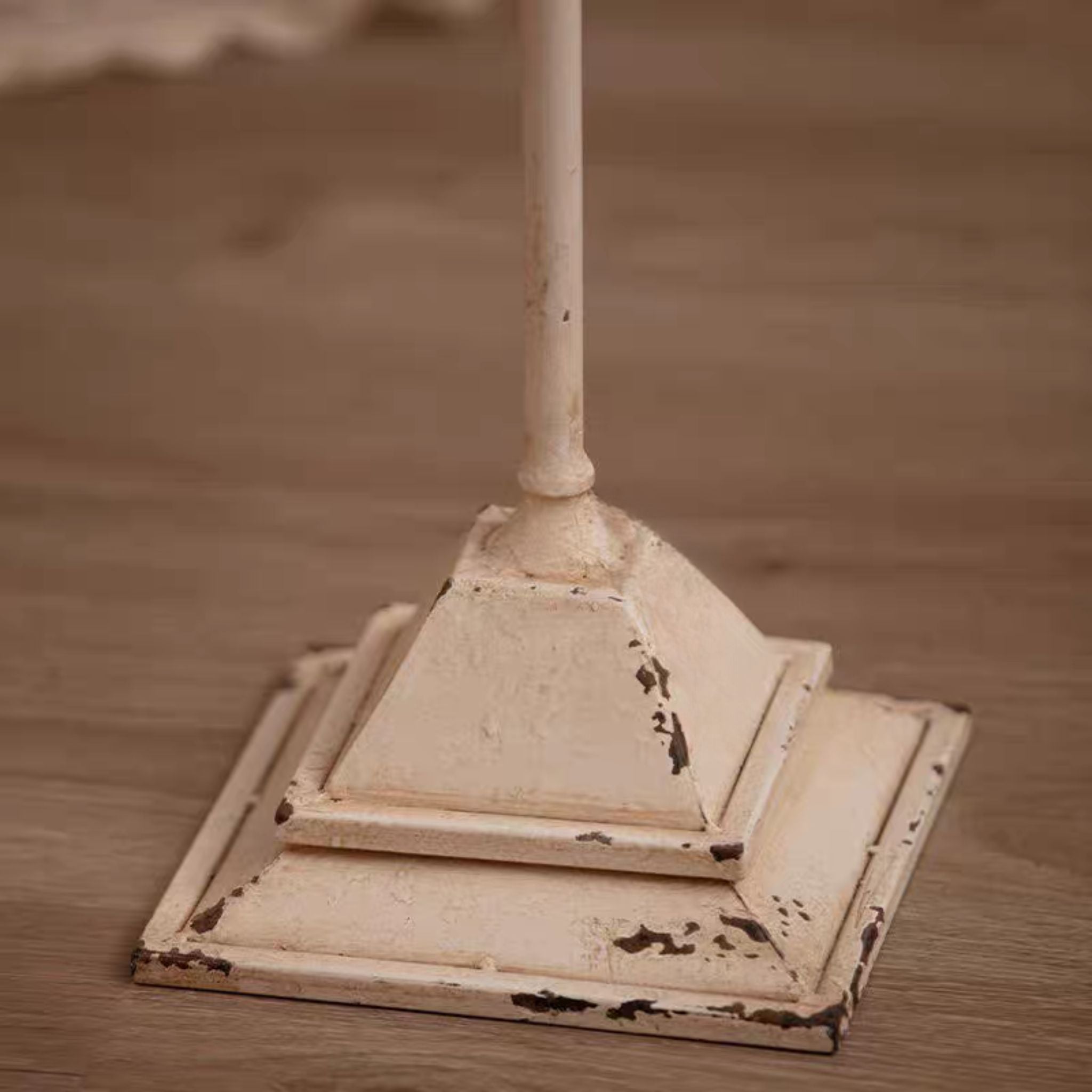 Close-up of the stepped square base and turned stem showing the worn distressed cream finish.