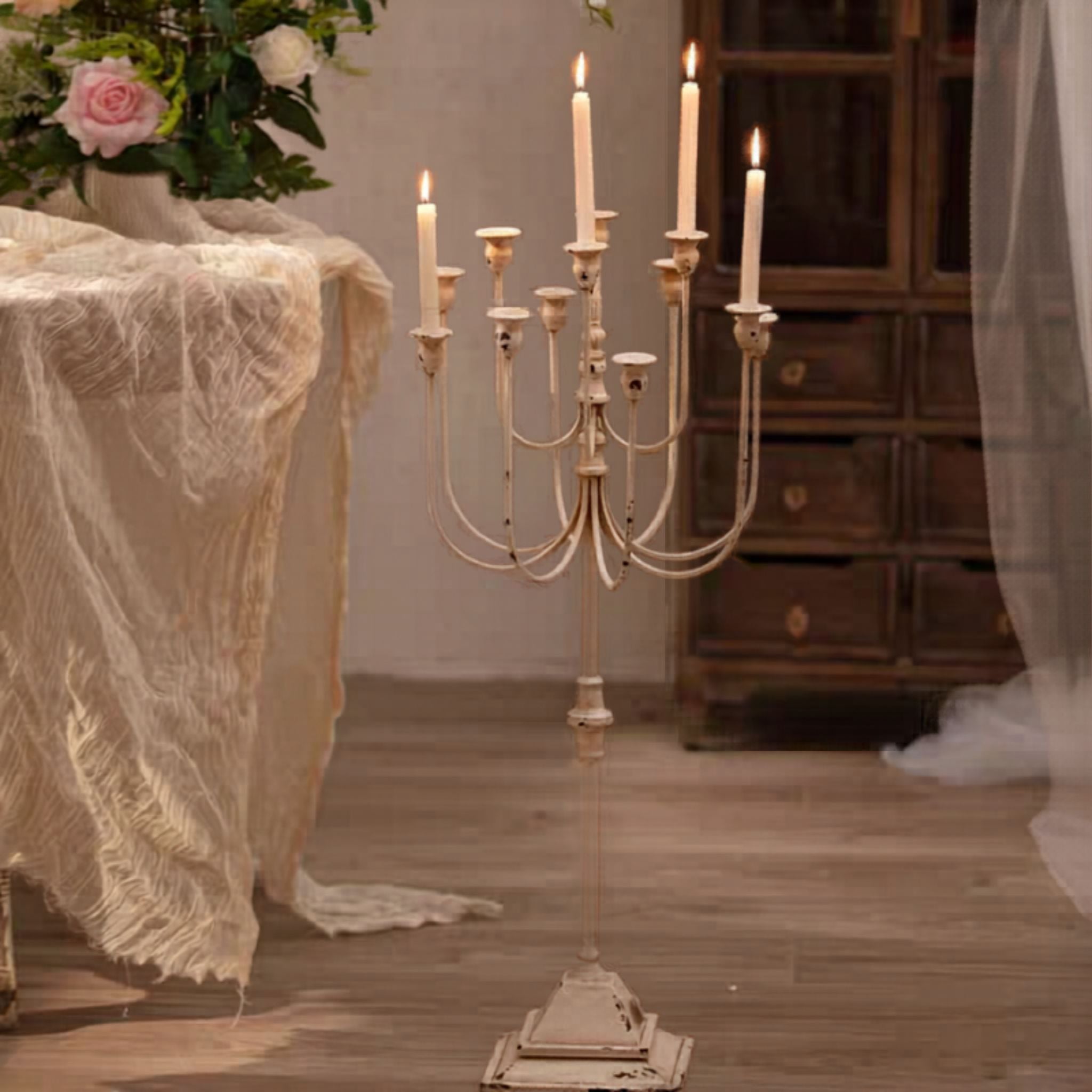 Tall floor candelabra lit beside a draped table and roses, showing its height on the floor.