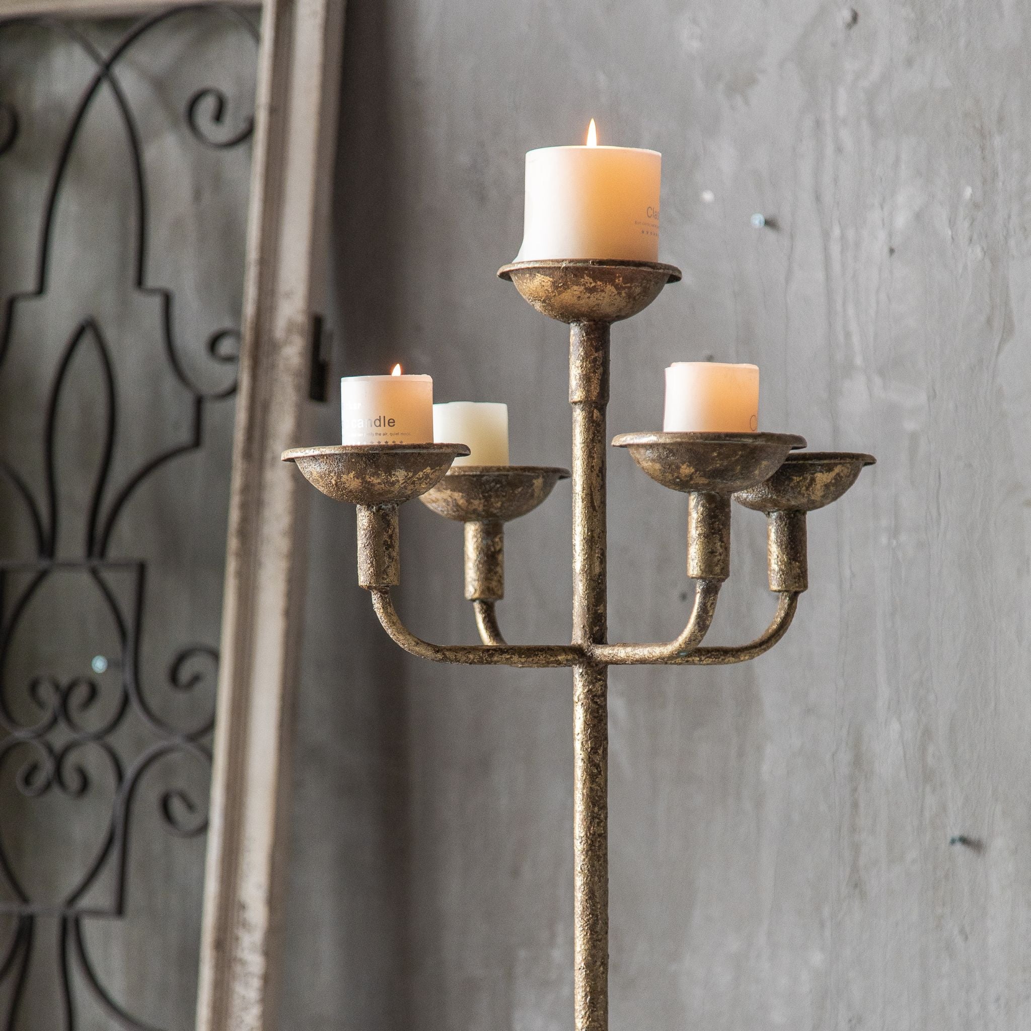 Close-up of the Florence candelabra head showing five cups holding pillar candles, one raised centre cup and four lower arms, in an antique gold finish worn over a darker base.