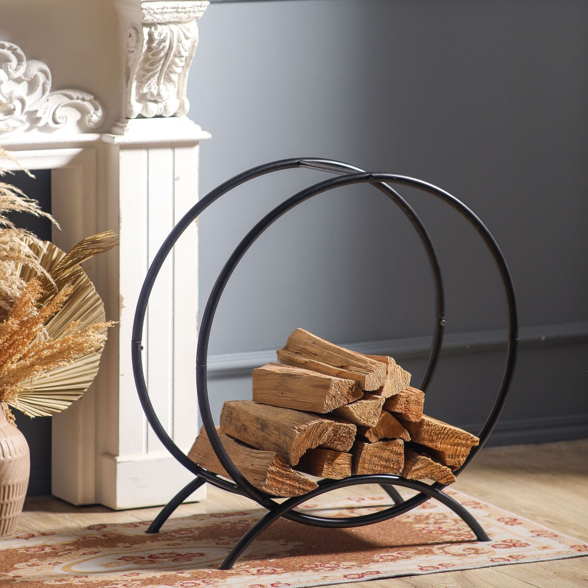 Emeric circular matte black firewood log hoop loaded with split logs beside a fireplace.