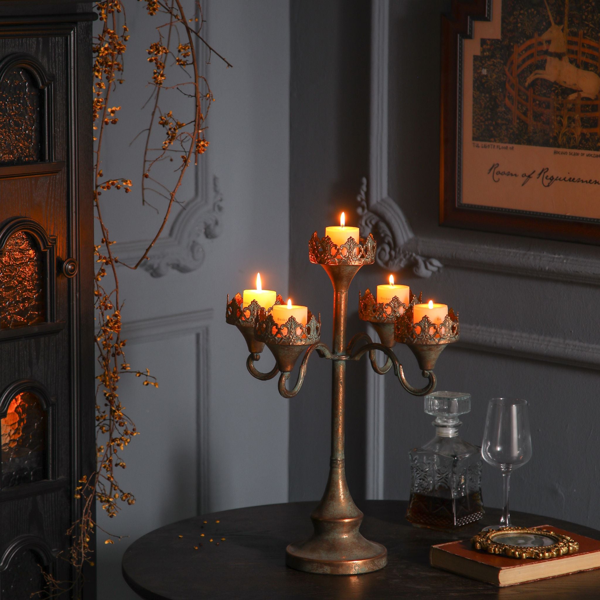 Corrine five-light antique gold candelabra with crown filigree collars, lit pillar candles, styled on a dark table with a decanter.