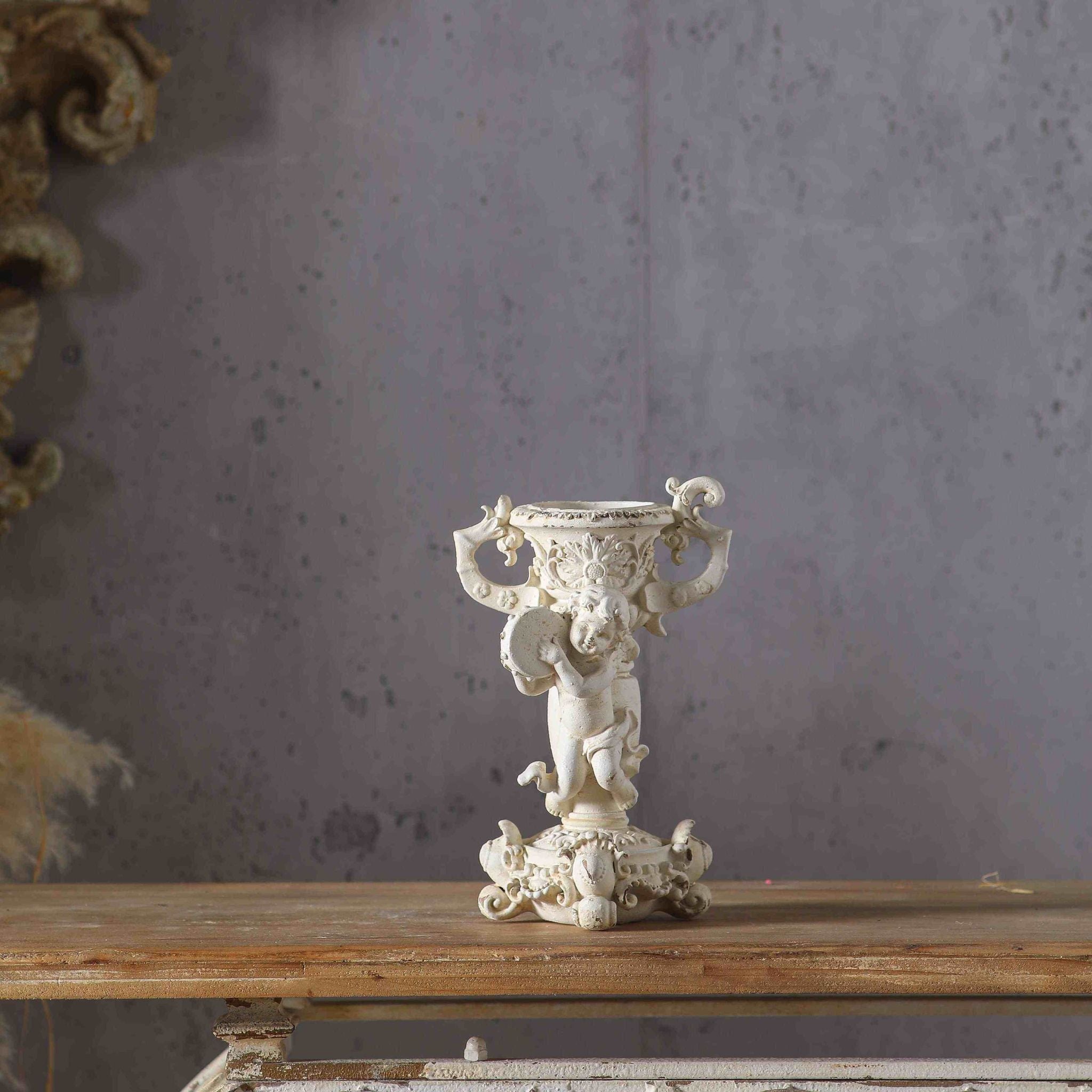 Claude French Provincial cherub candle holder in antique cream, a putto holding a tambourine beneath an urn candle cup