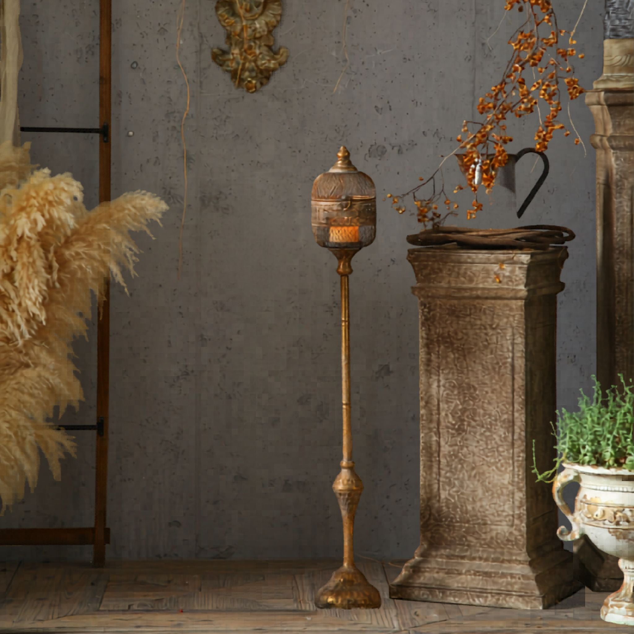 Celine French Provincial standing candle lantern in antique gold aged metal, pierced diamond mesh head on a tall turned pedestal, lit candle inside, styled beside a stone plinth.
