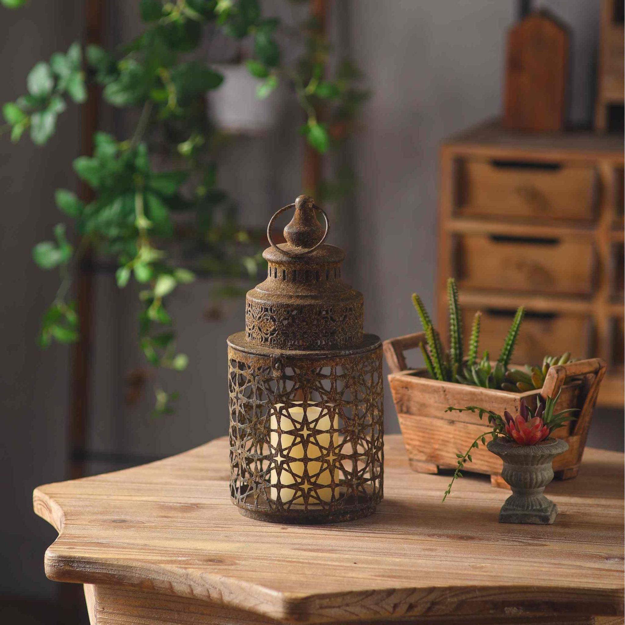 Rueben French Provincial Moroccan star-pierced lantern in weathered rust aged metal, lit candle inside, on a timber table with succulents and greenery.