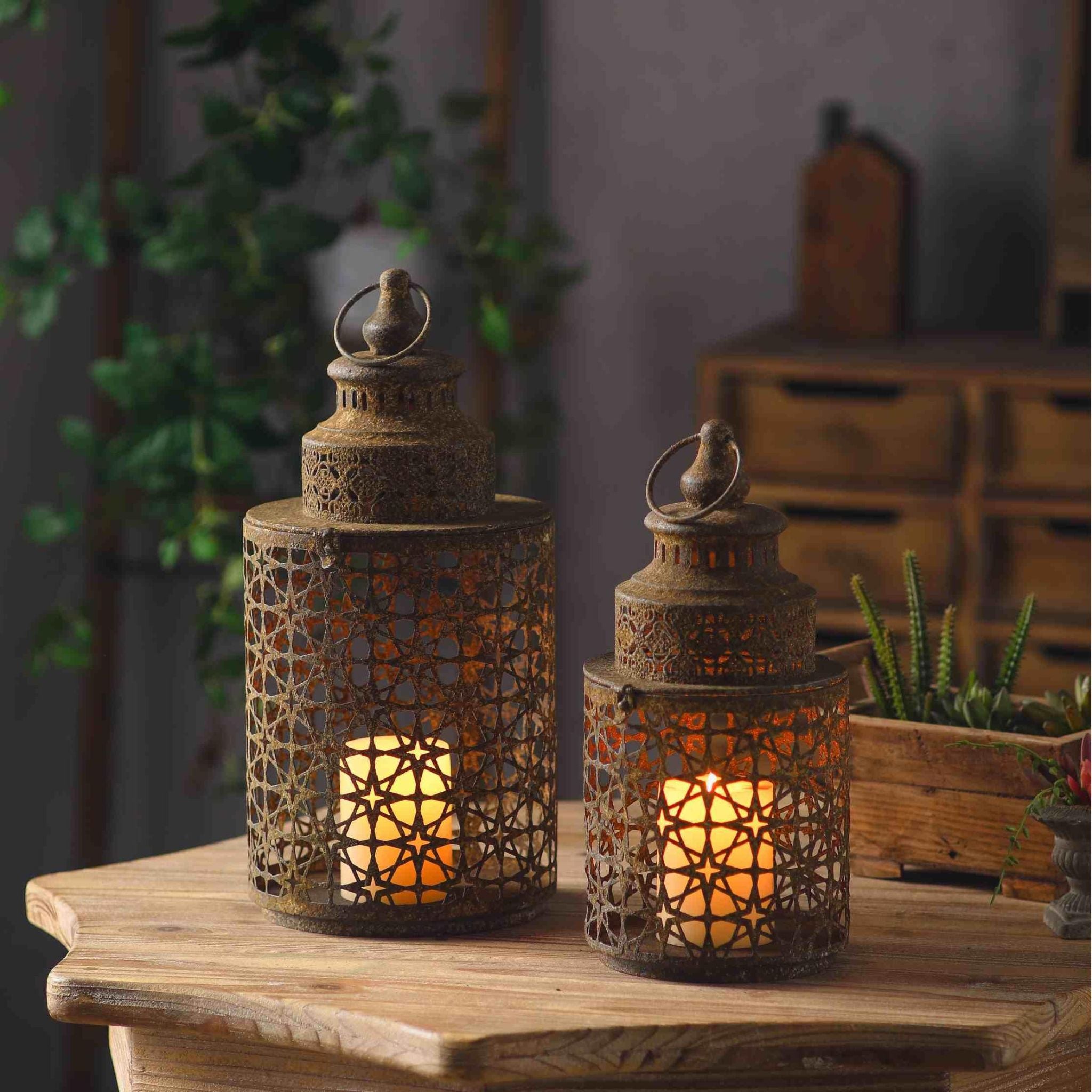 Yannick French Provincial Moroccan star-pierced lantern in weathered rust aged metal, lit candle inside, on a timber table with succulents and greenery.