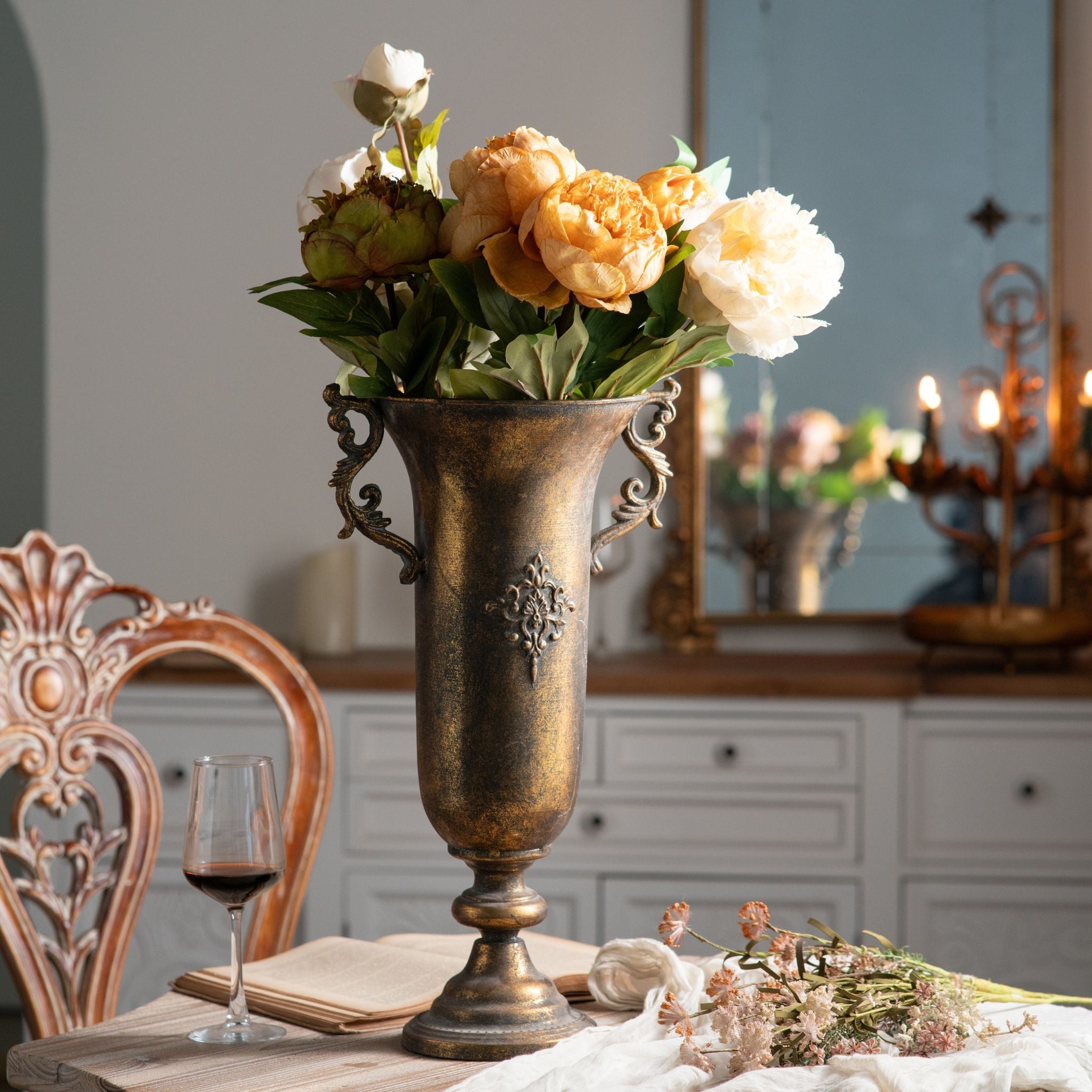 Coralie French Provincial urn vase in aged gold metal with scroll handles, filled with peonies on a dining table