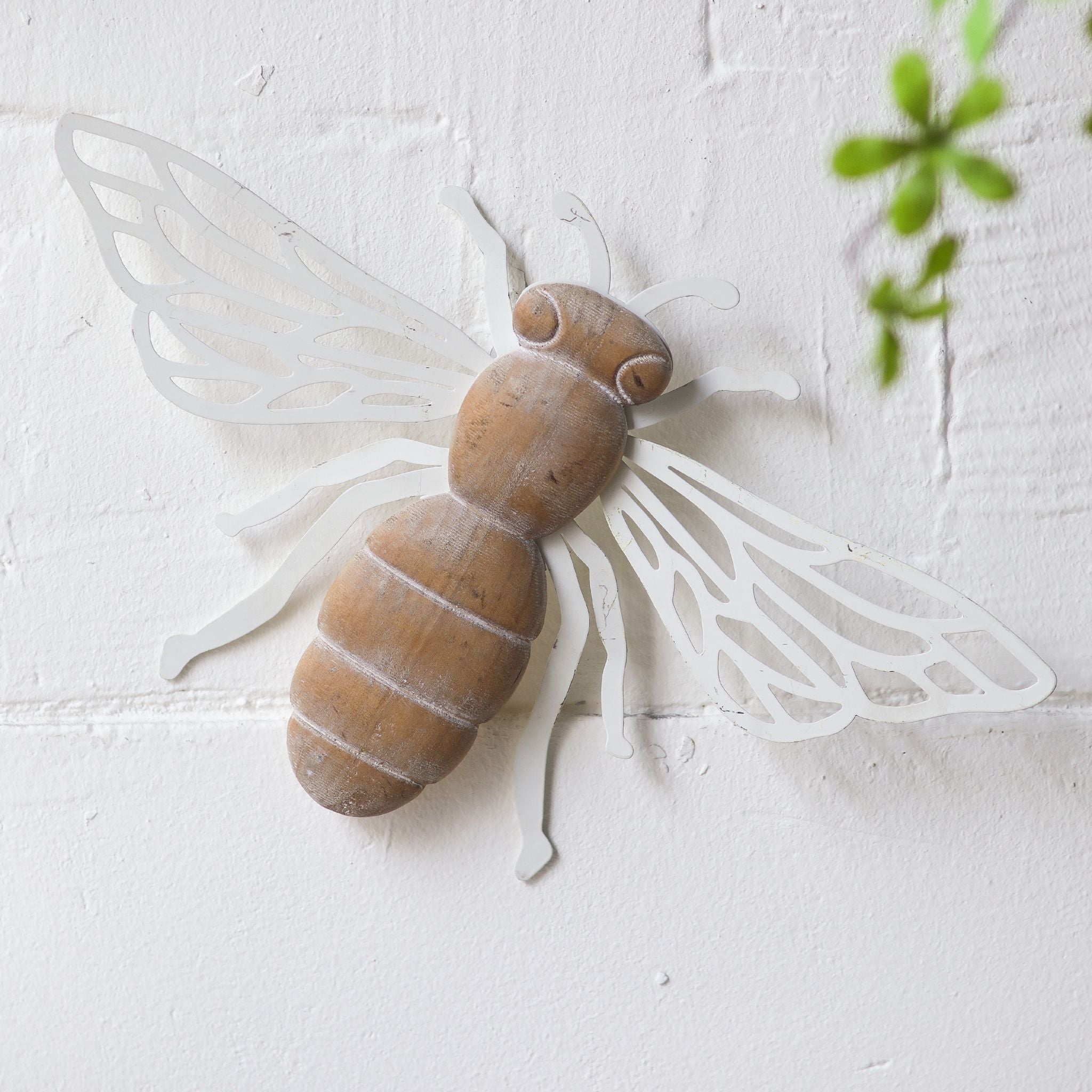 Honey French Provincial bee wall decor with distressed wood body and laser-cut antique white iron wings, mounted solo on a textured white brick wall. Hero.