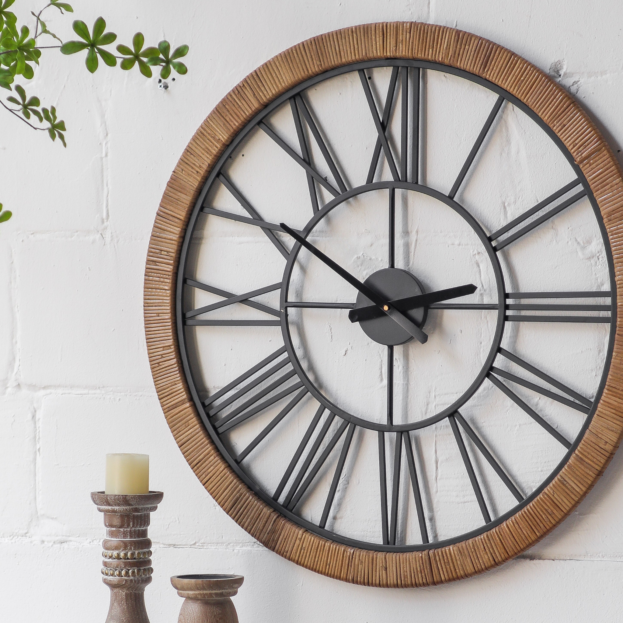 Hugo wall clock at an angled close-up showing the rattan-wrapped frame texture and Roman numeral detail, with wood candle holders below