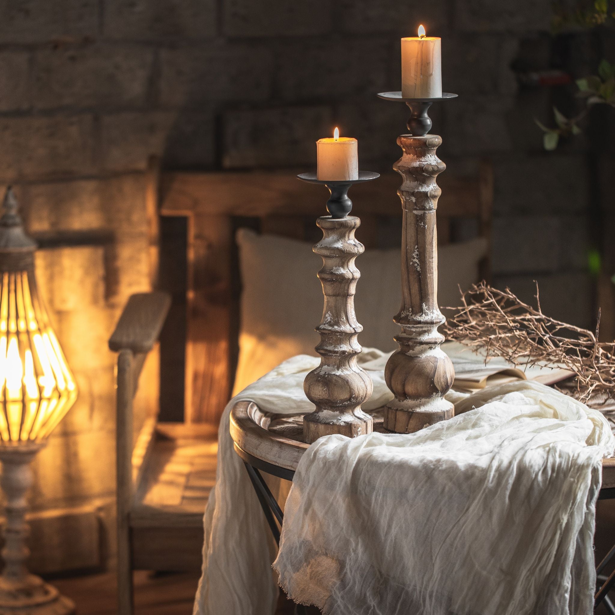 Jean French Provincial pillar candle holder in distressed white turned timber with an aged metal dish, lit pillar candle, shown shorter in front of the taller size.