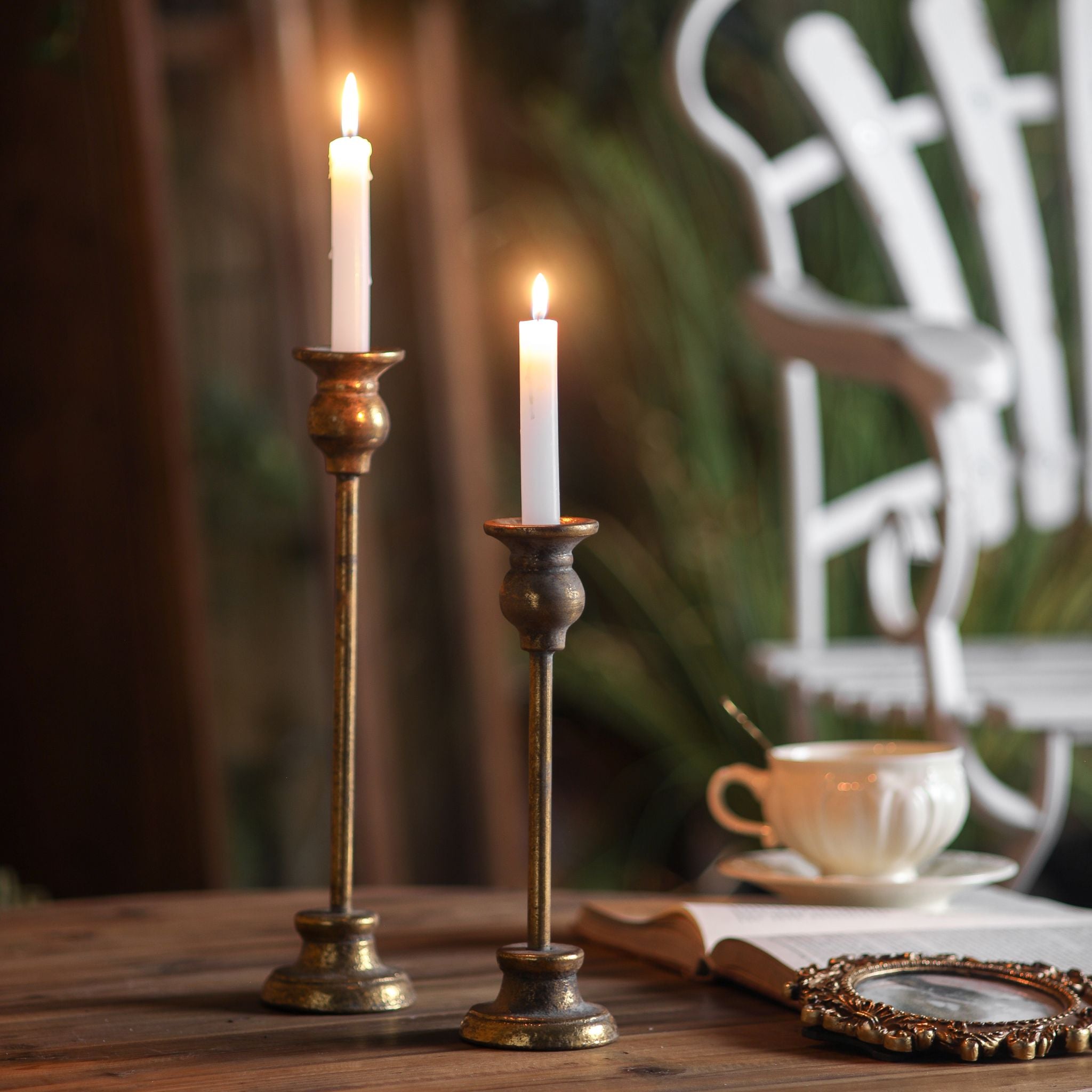 Karine French Provincial taper candlestick set, two aged gold metal holders of different heights with white taper candles on a timber table