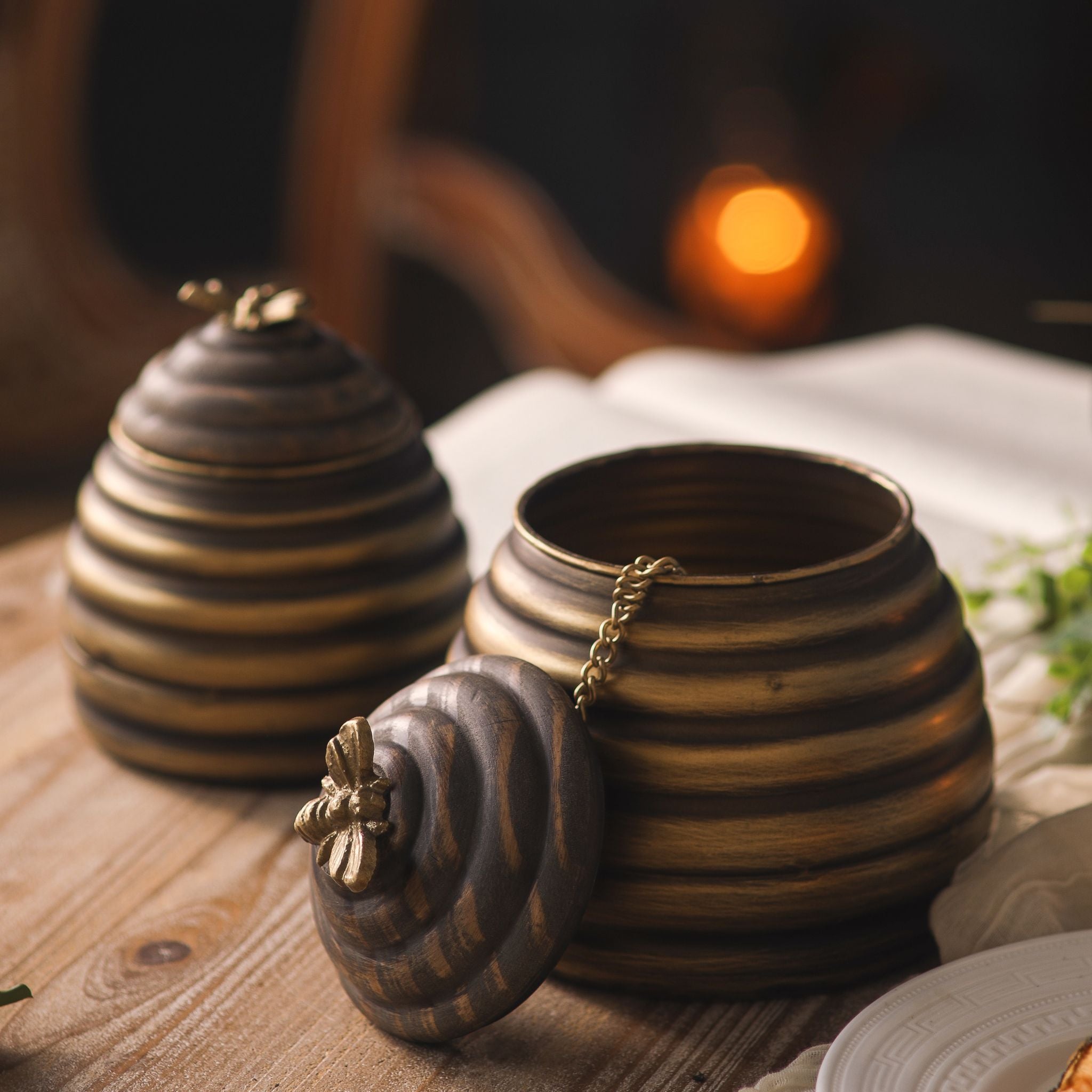 Leonie beehive pots with one timber lid lifted off, showing the hollow metal inside and the brass chain joining lid to pot.