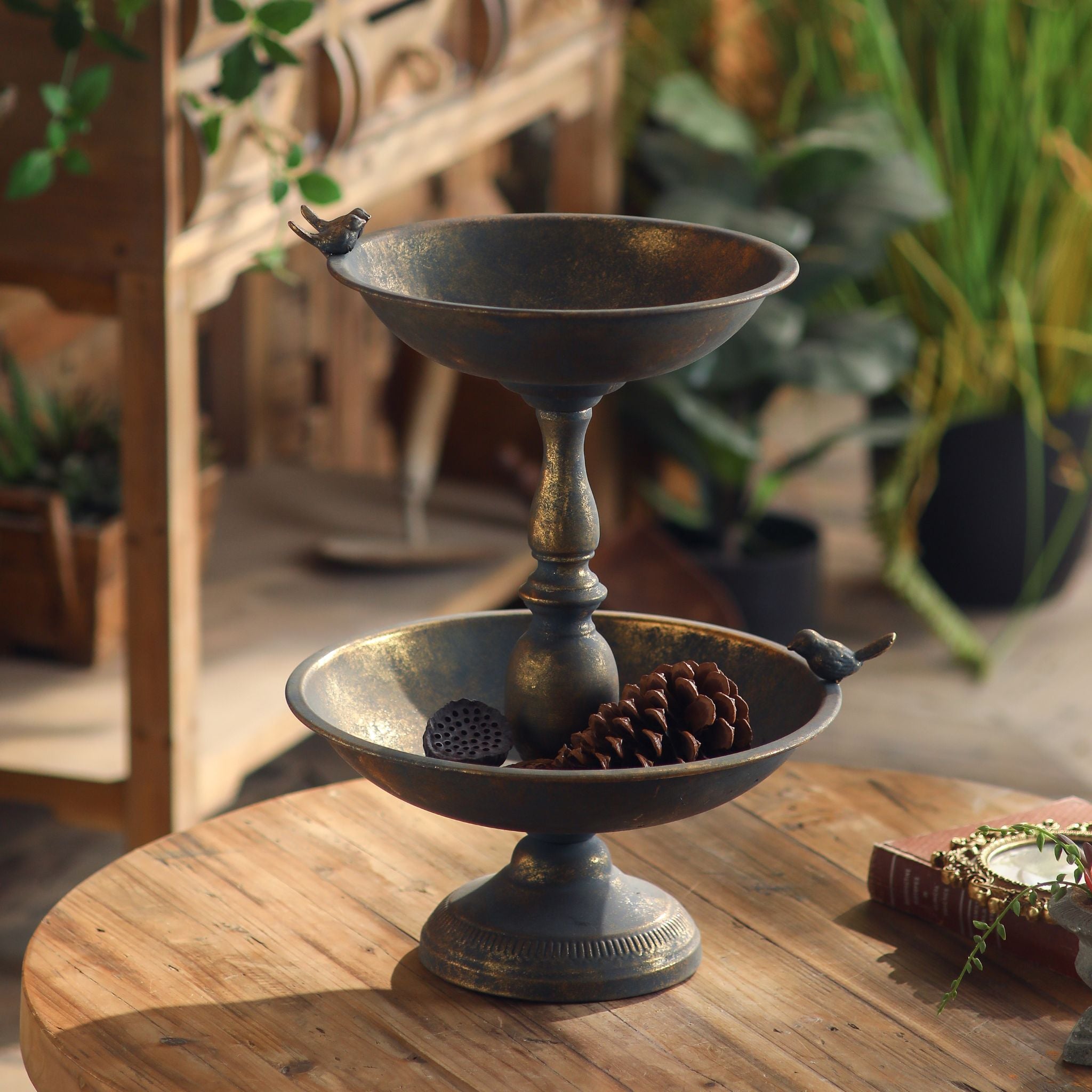 Lorraine French Provincial two tier dish stand in antique gold metal with a small bird perched on each rim, on a timber table. Hero.
