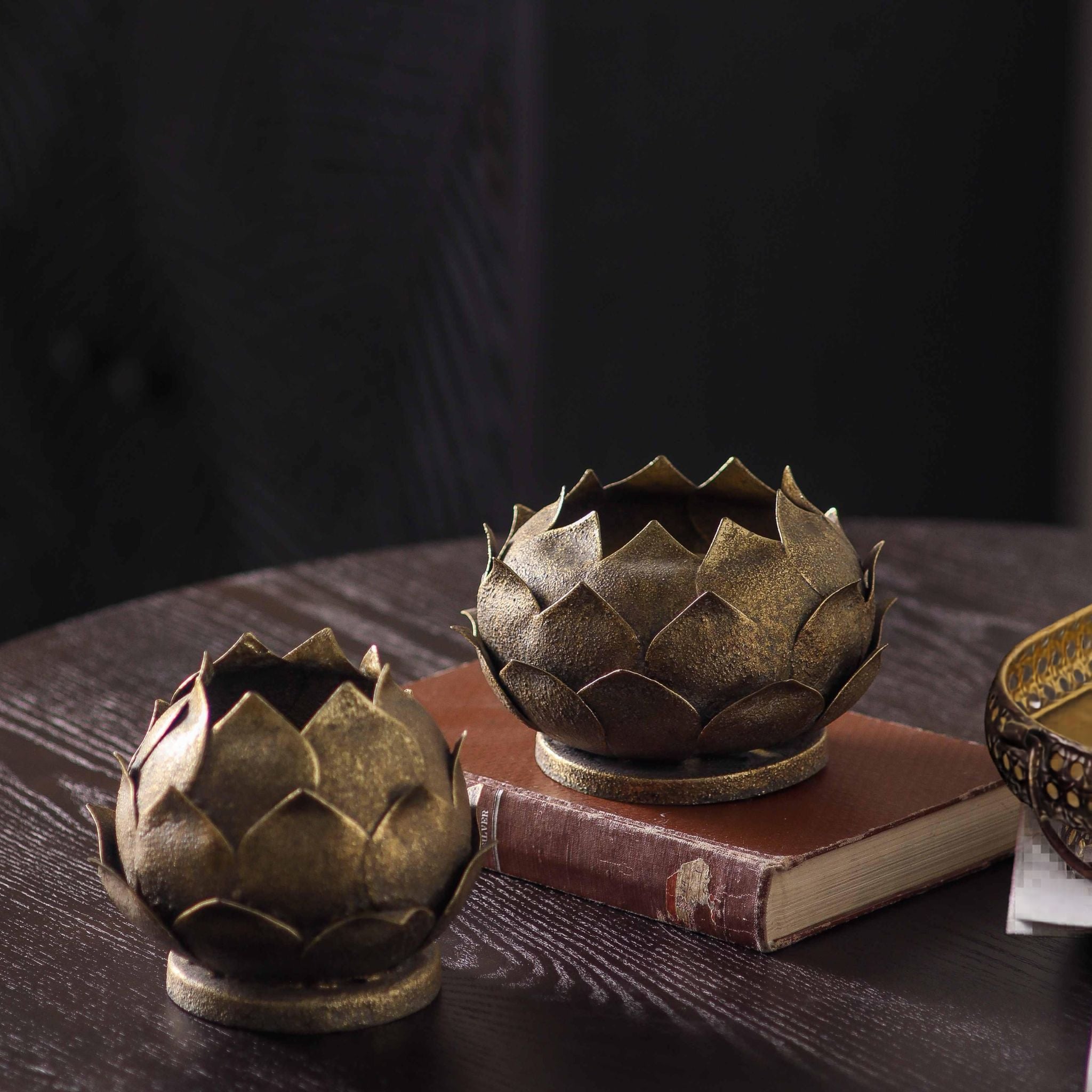 Two lotus tealight holders in aged metal, one open bloom and one closed flower, antique gold finish.