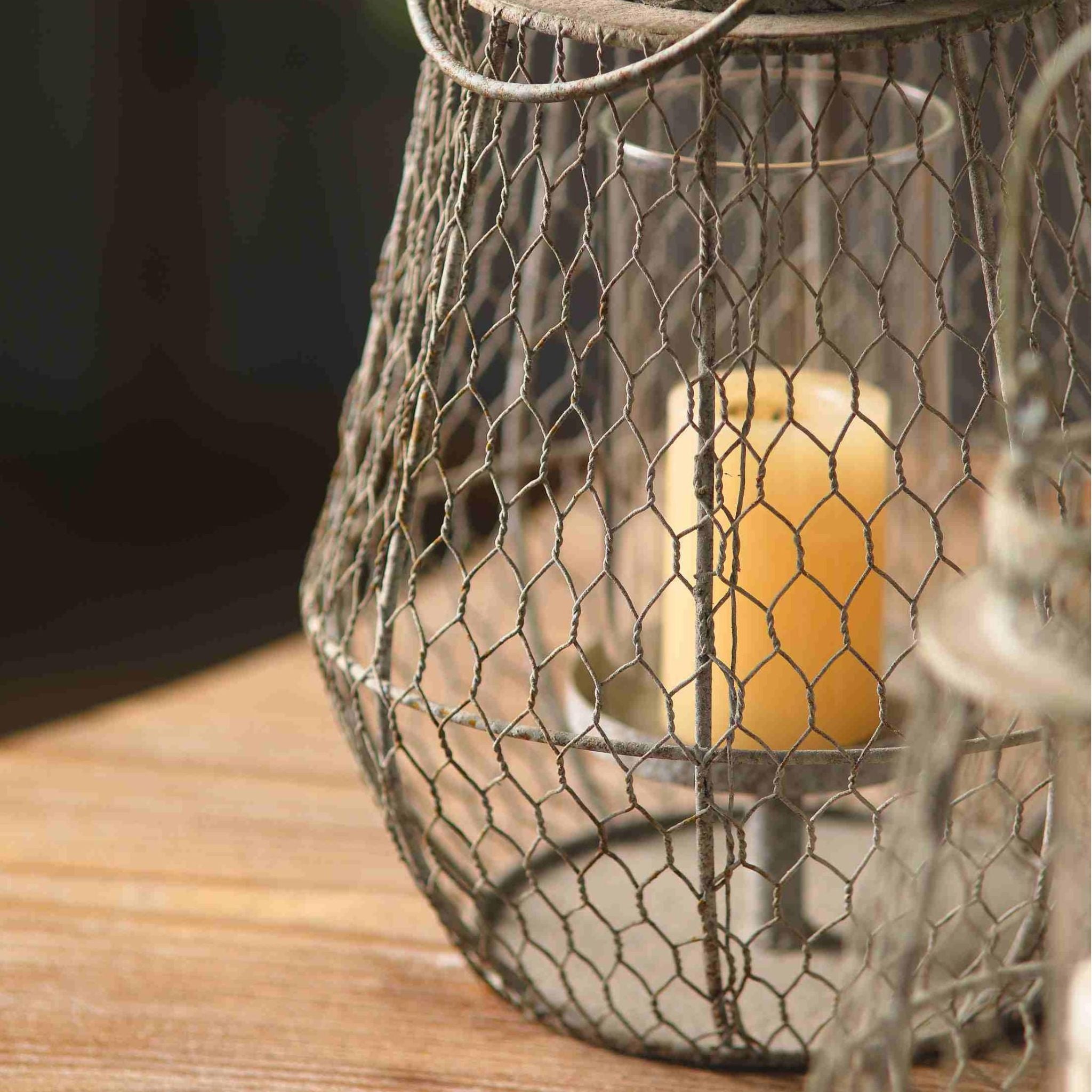 Close detail of the Louise lantern's woven wire mesh and clear glass insert holding a lit pillar candle.