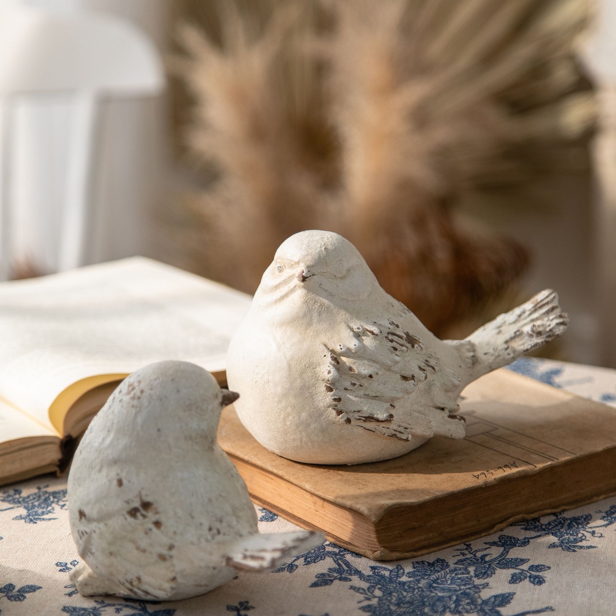 Lucas whitewashed bird figurines, set of two, styled on a blue toile cloth with a teacup and an open book