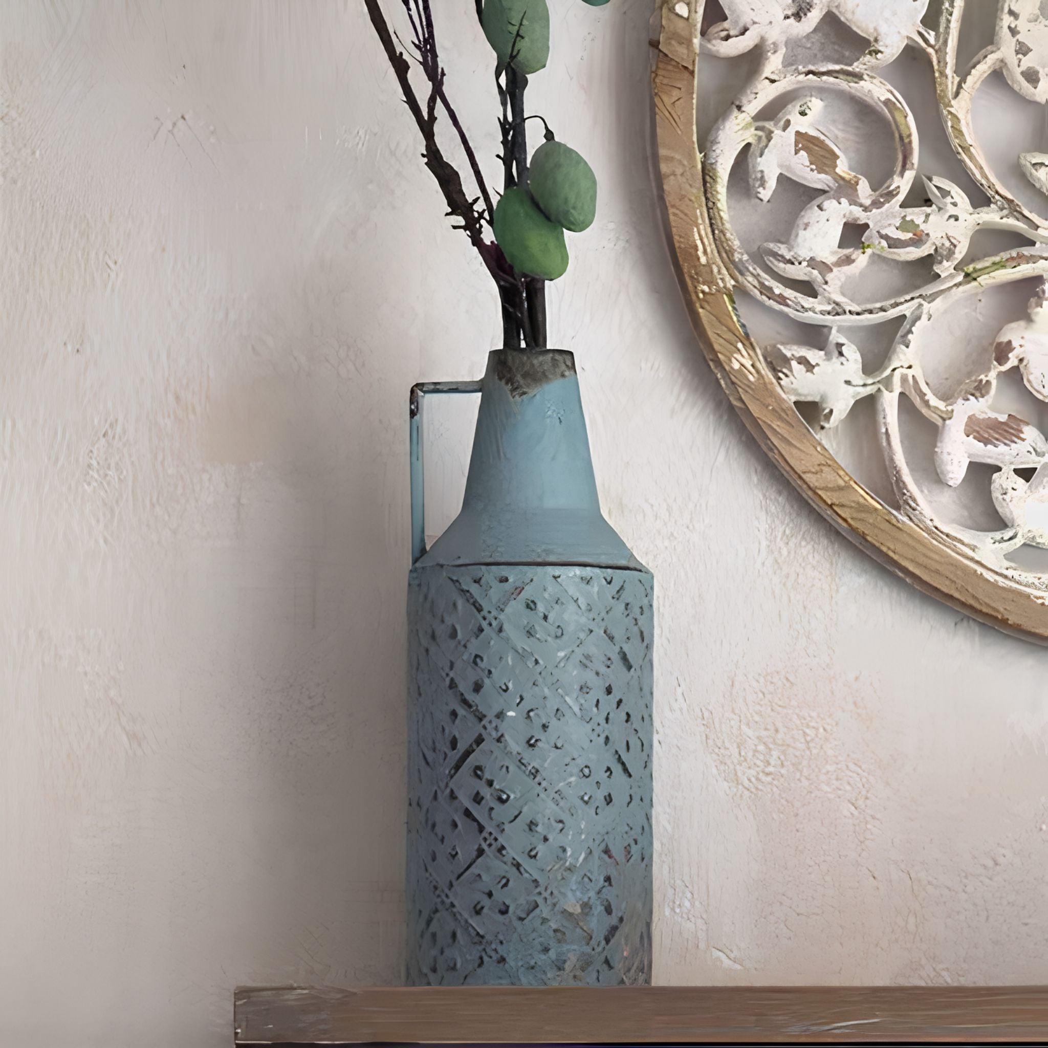 Marianne blue bottle vase holding dried stems and eucalyptus, beside a carved round wall art Amber
