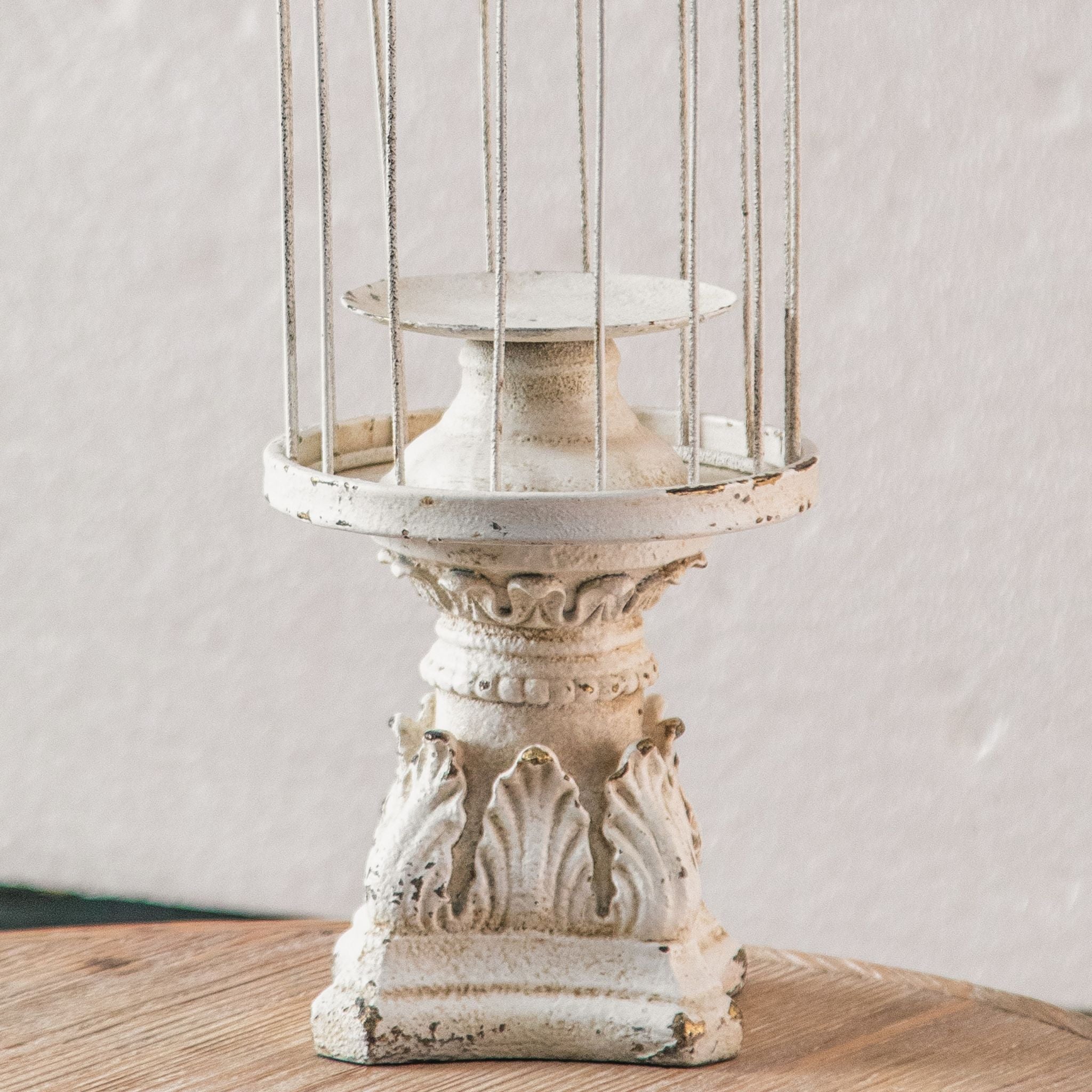 Close-up of the Matheo candle plate, turned pedestal and acanthus leaf base in distressed white worn to terracotta.