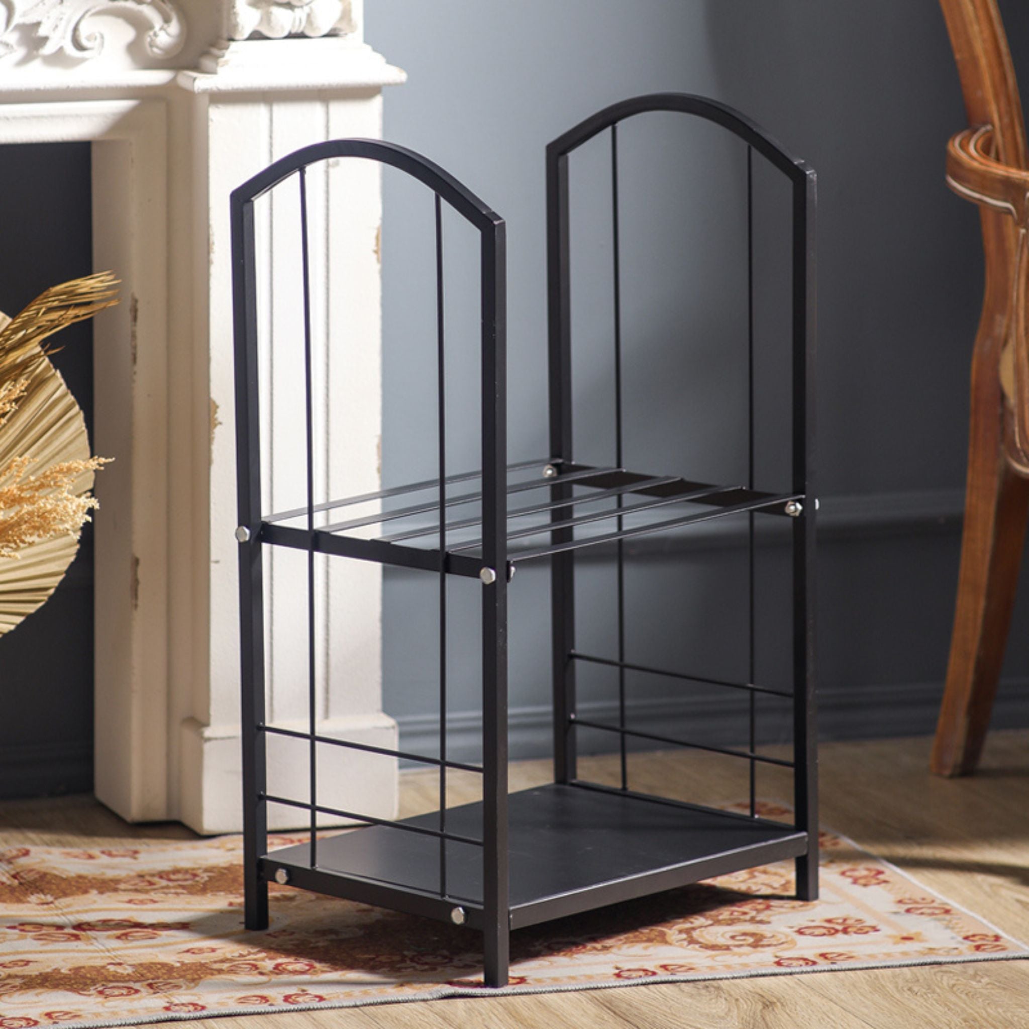 The Didier matte black two-tier log rack shown empty, with arched sides, beside a white fireplace.