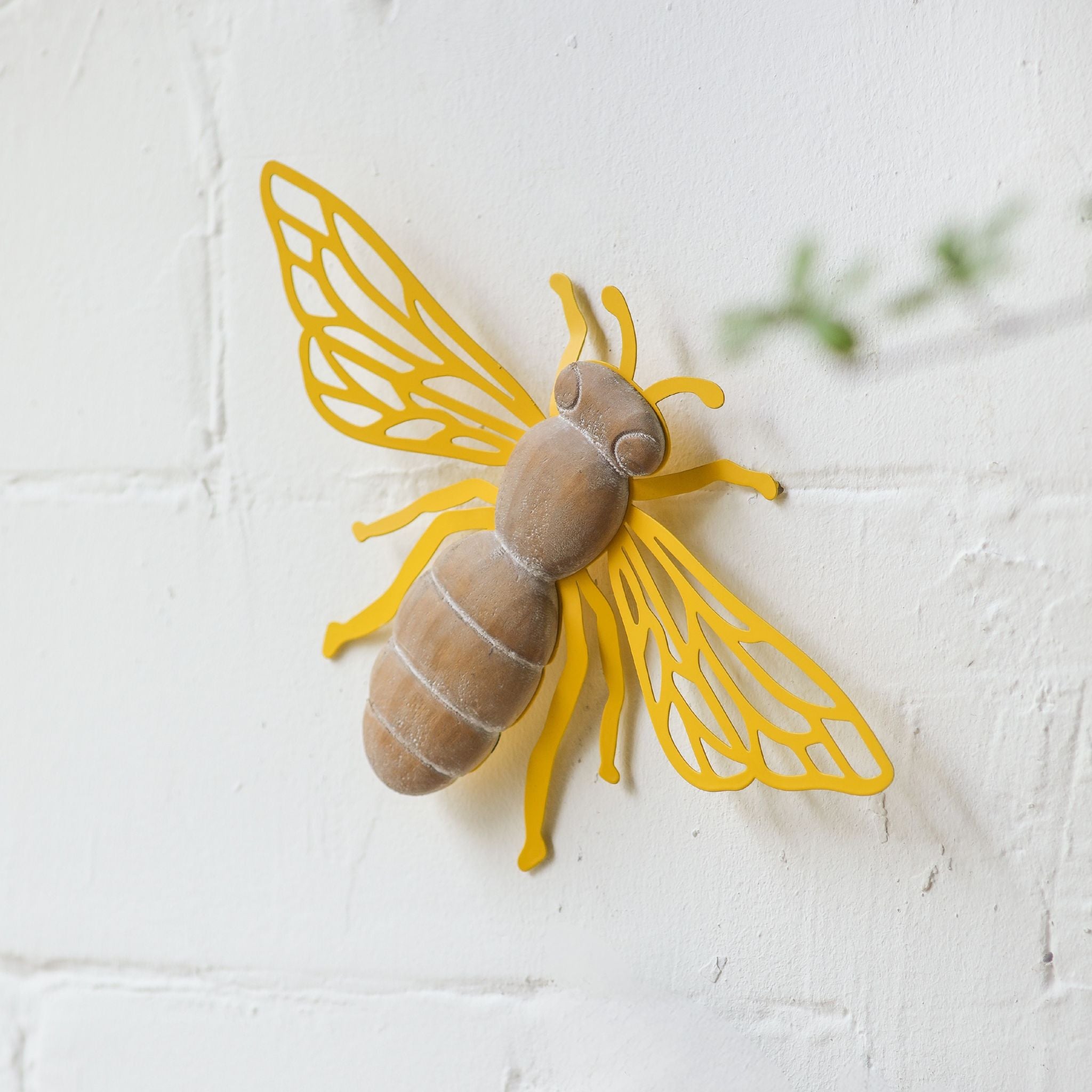 Maya French Provincial bee wall decor with distressed wood body and laser-cut yellow iron wings, mounted solo on a textured white wall. Hero