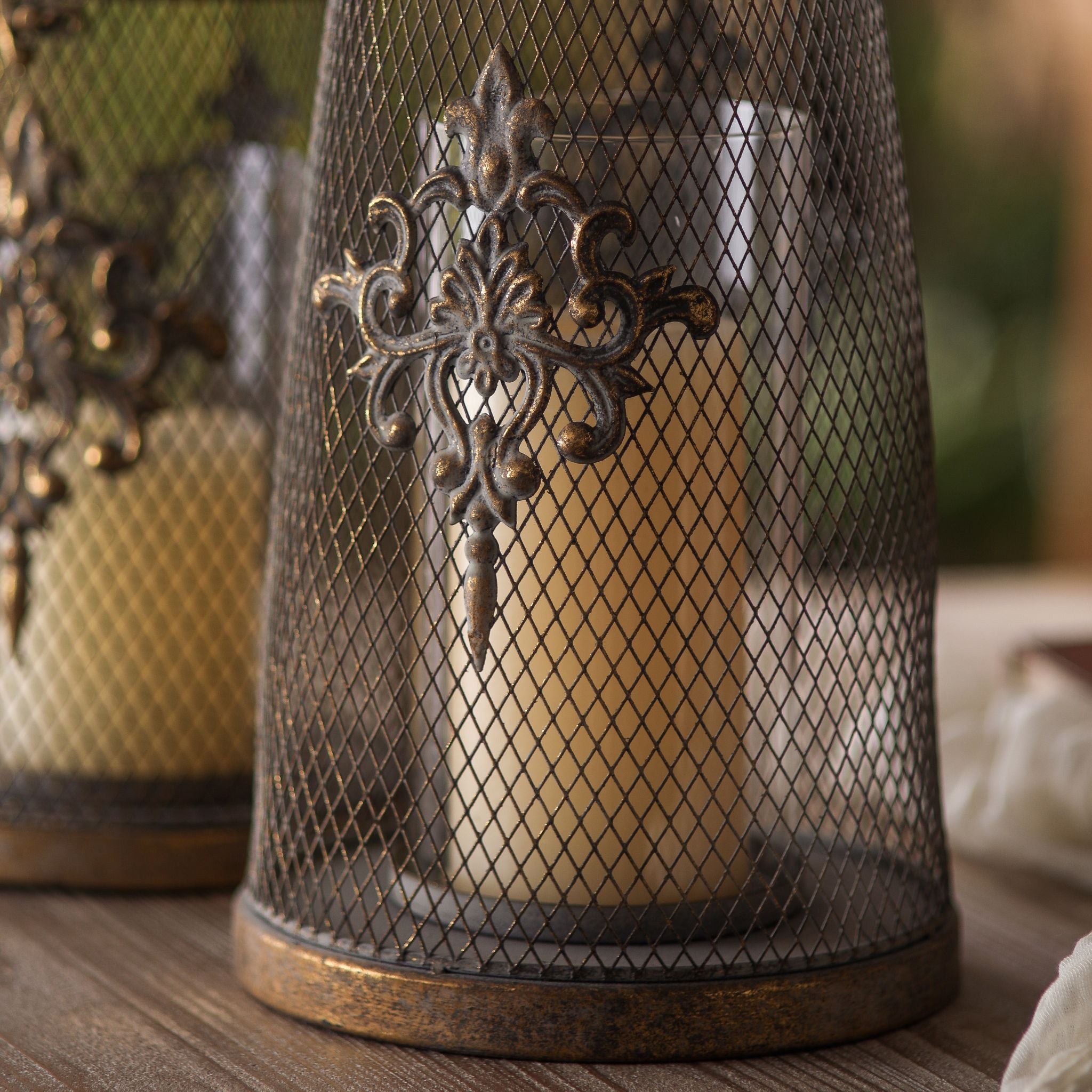 Stephanie tall French Provincial candle lantern in aged gold mesh with a glass insert, lit on a timber table at golden hour