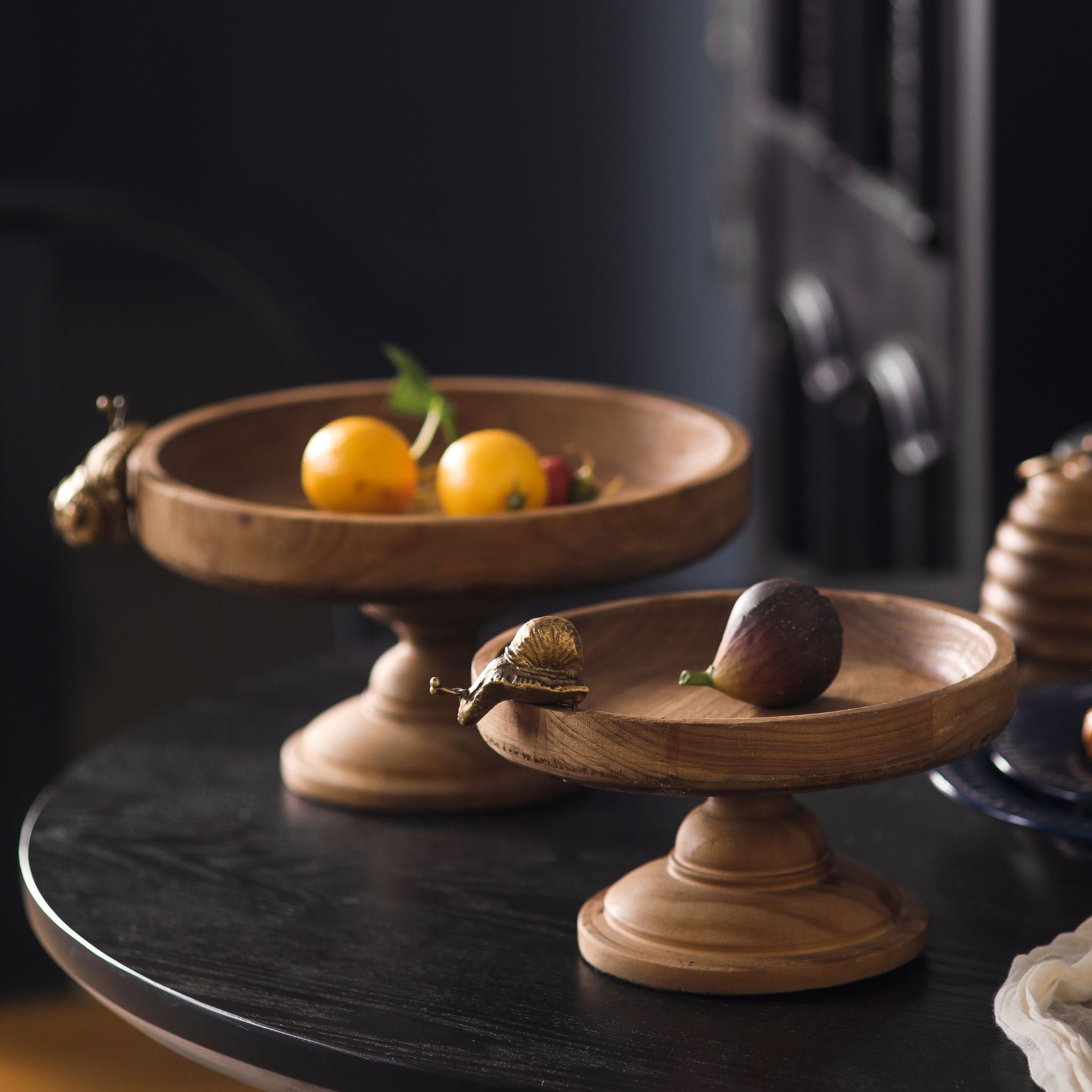 Two footed wooden trays in graduated sizes shown together on a dark table.