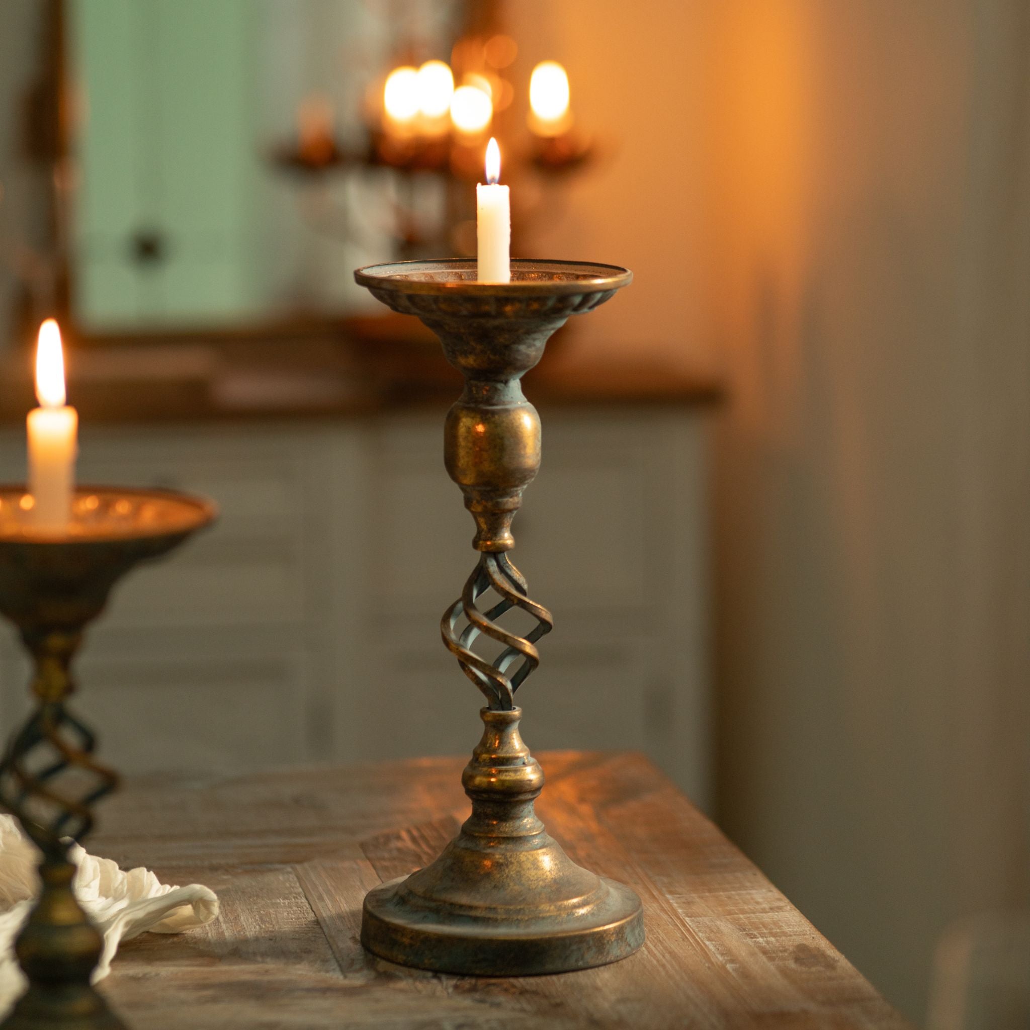 Michel candle holder lit and styled on a sideboard with a mirror and candle sconce behind, antique gold and verdigris finish.