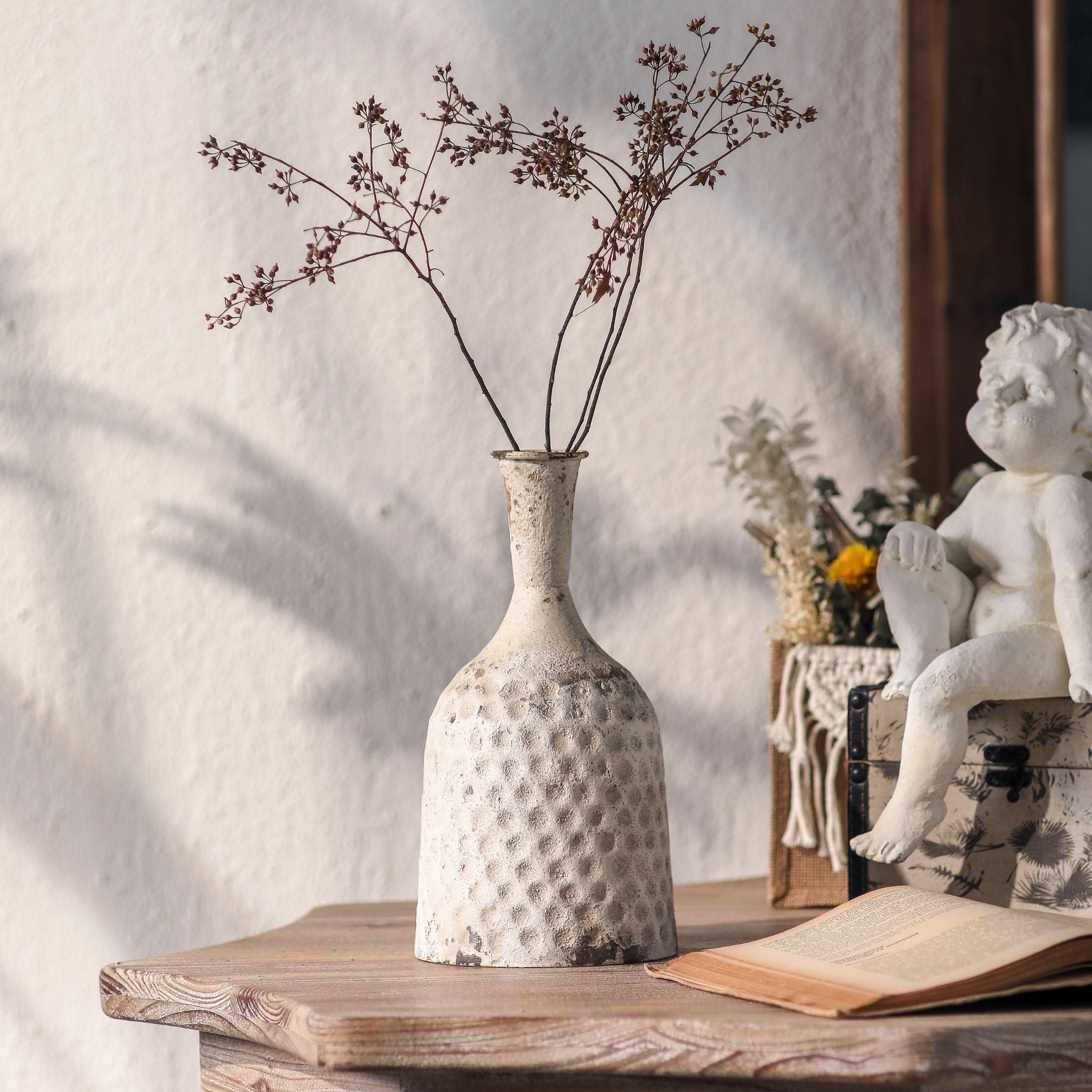 Michelle hammered-metal bottle vase in distressed white, styled with dried branches on a table. Hero.