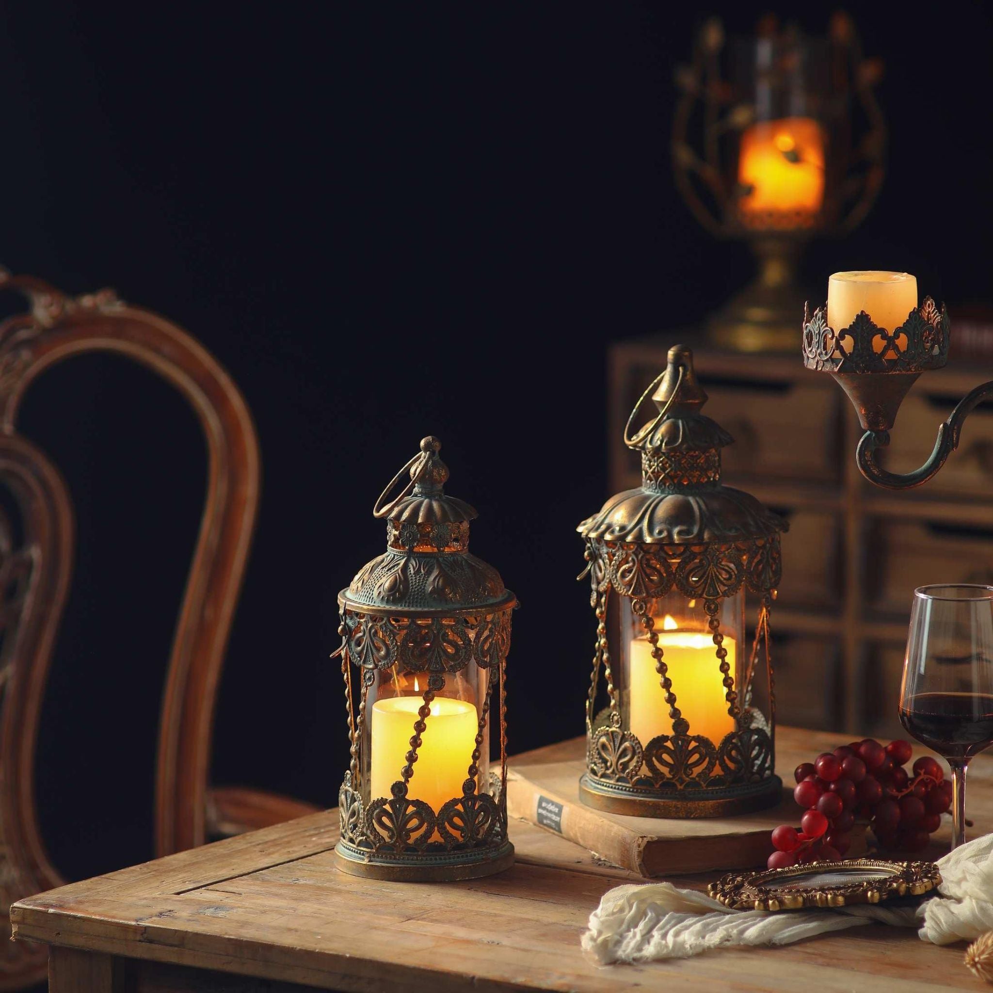 Mylan and the taller Mael filigree lanterns lit on a timber table, styled with grapes, an old book and a glass of wine.