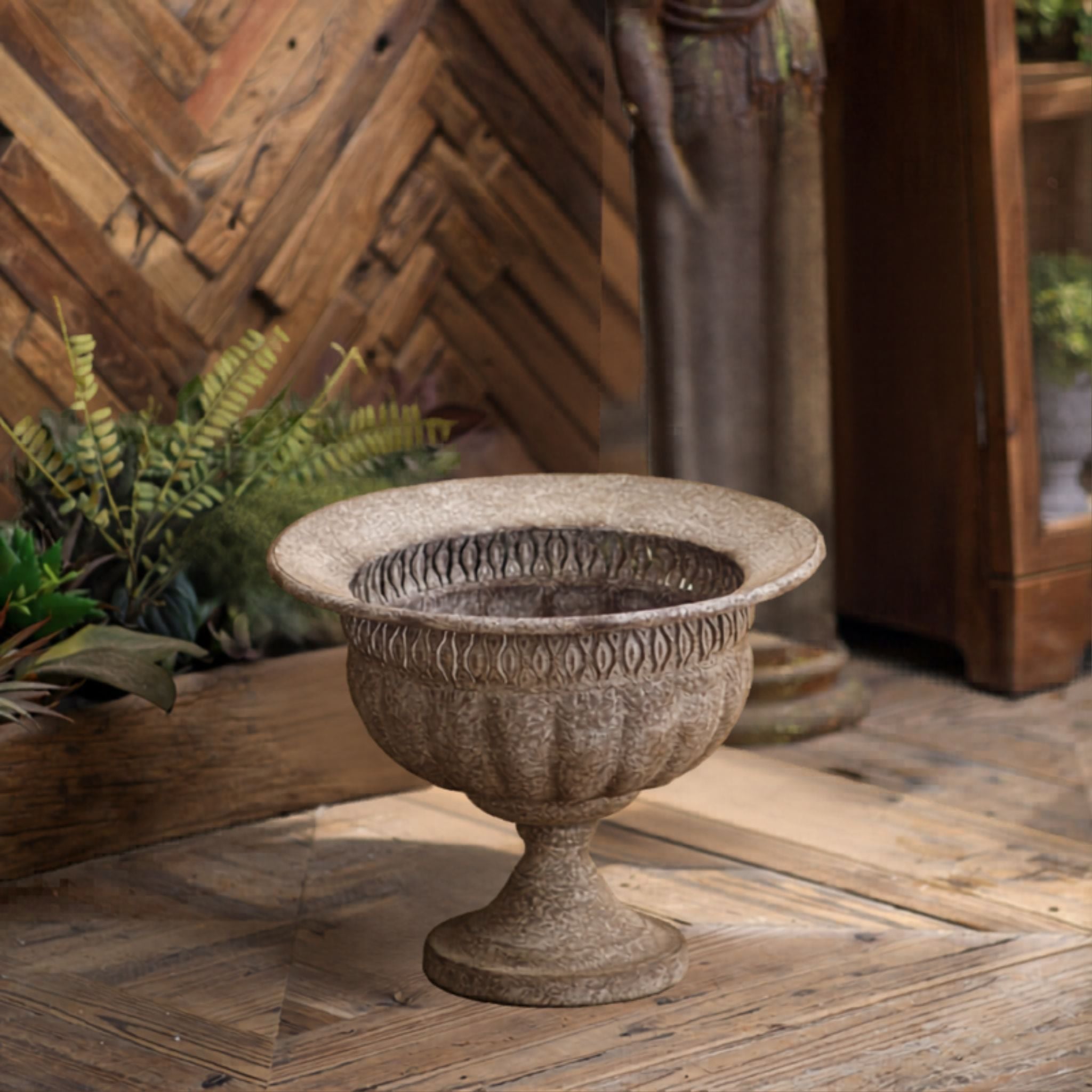 Myriam urn planter beside a fern in a rustic timber setting, full three-quarter view.