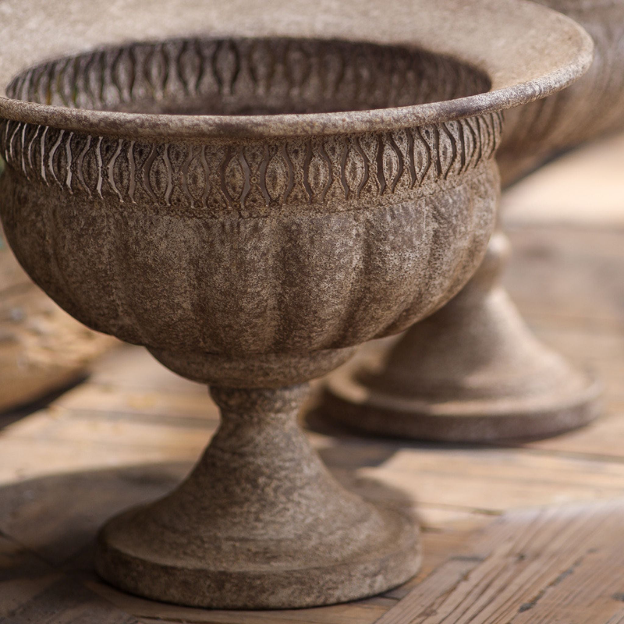 Close-up of the Myriam urn bowl and pedestal, fluted body and pierced rim band in an aged stone-look finish.
