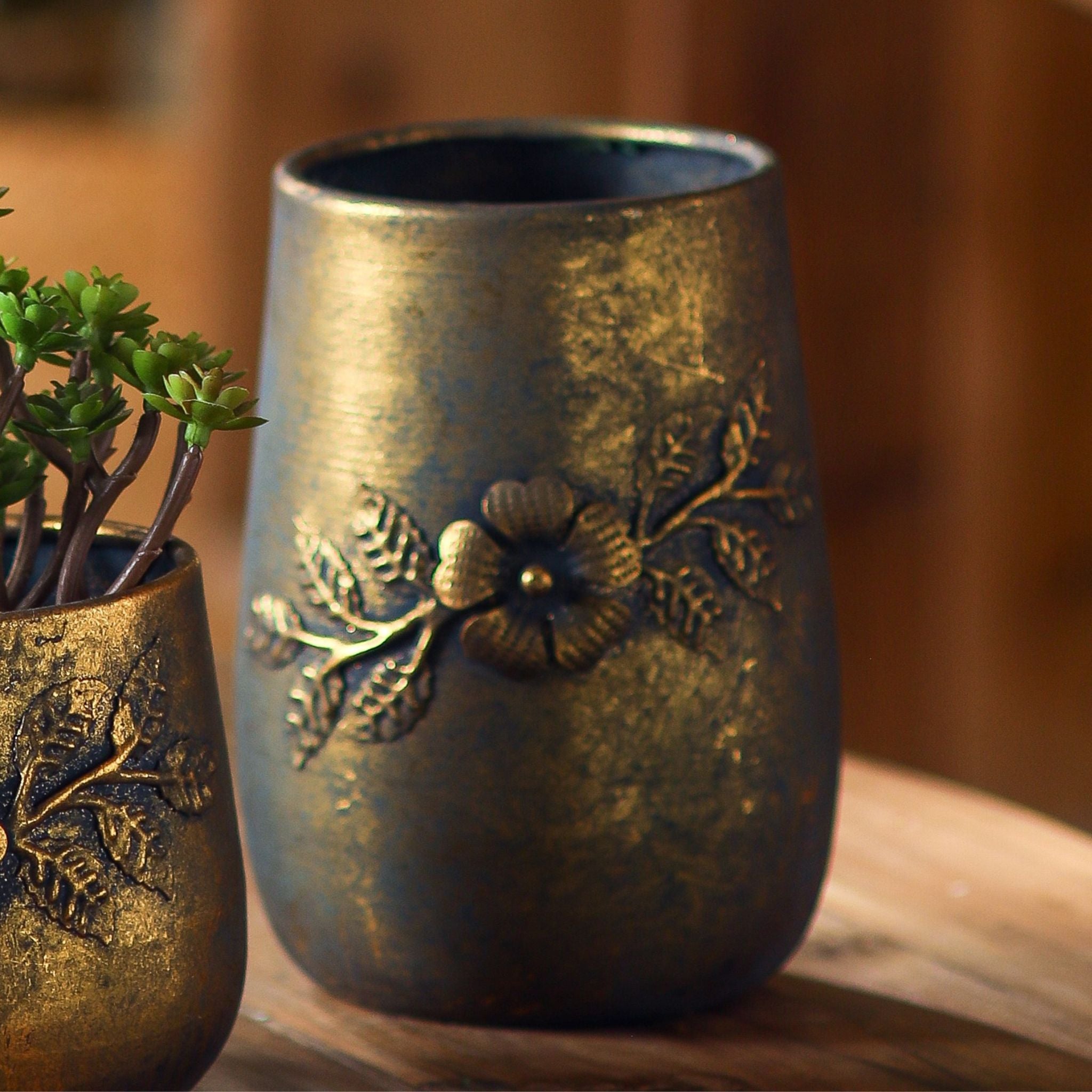 Normandy pot, detail of the raised gold flower and leafy branch on the antique-gold finish.