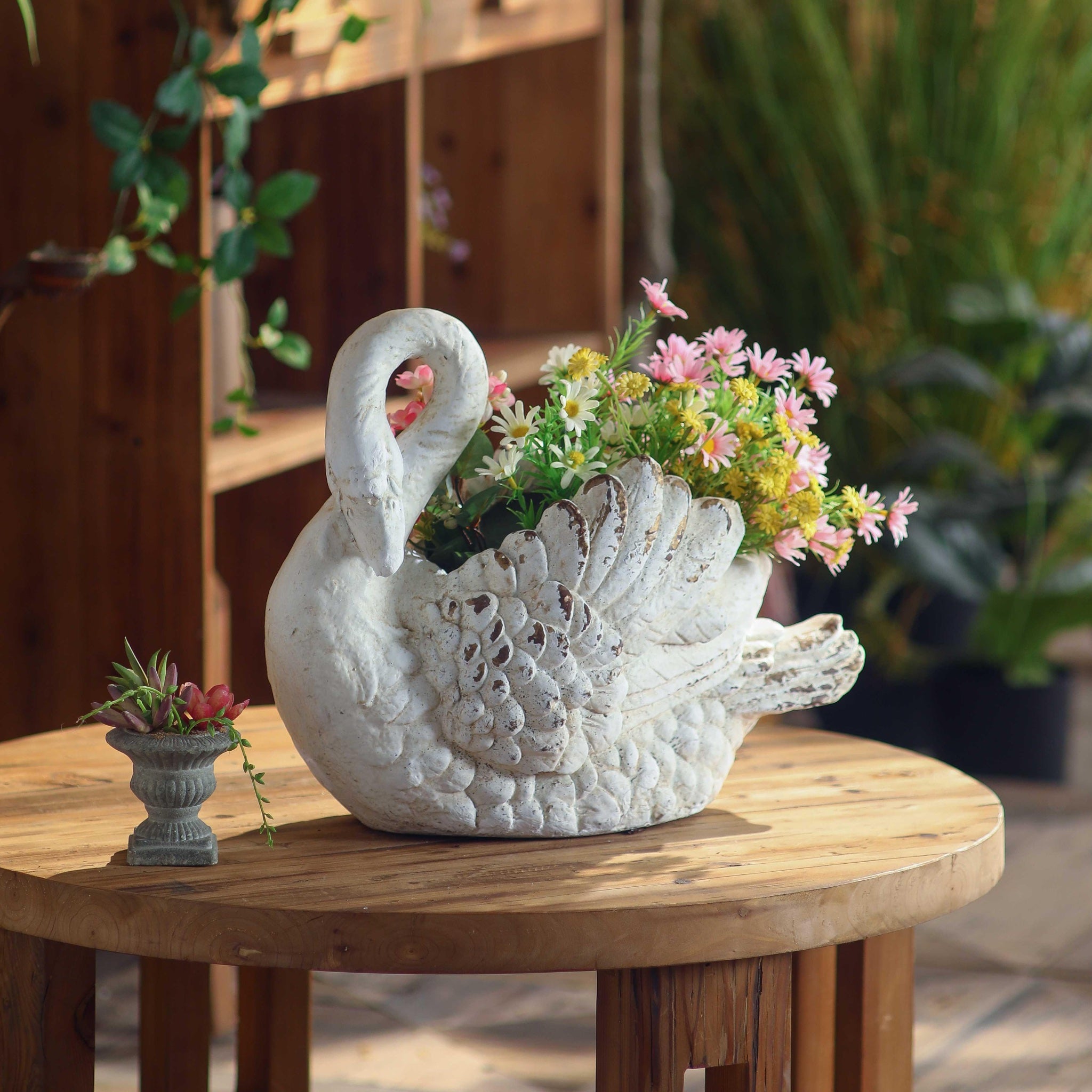 Odette French Provincial swan planter on timber table, styled with pink daisies and yellow blooms in a sunlit garden setting. Hero.
