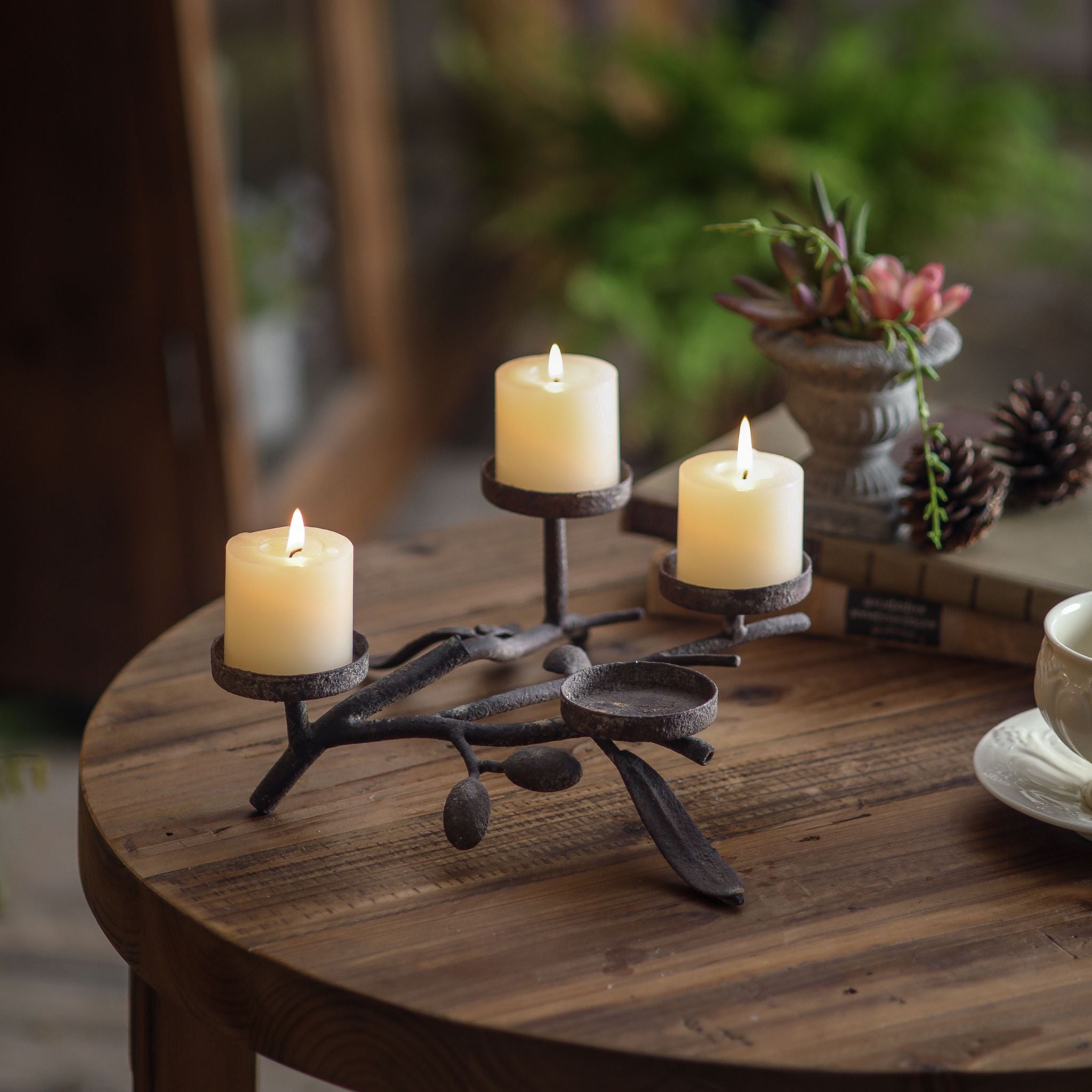 Olive branch candle centrepiece lit with three pillar candles, styled with greenery and pinecones.