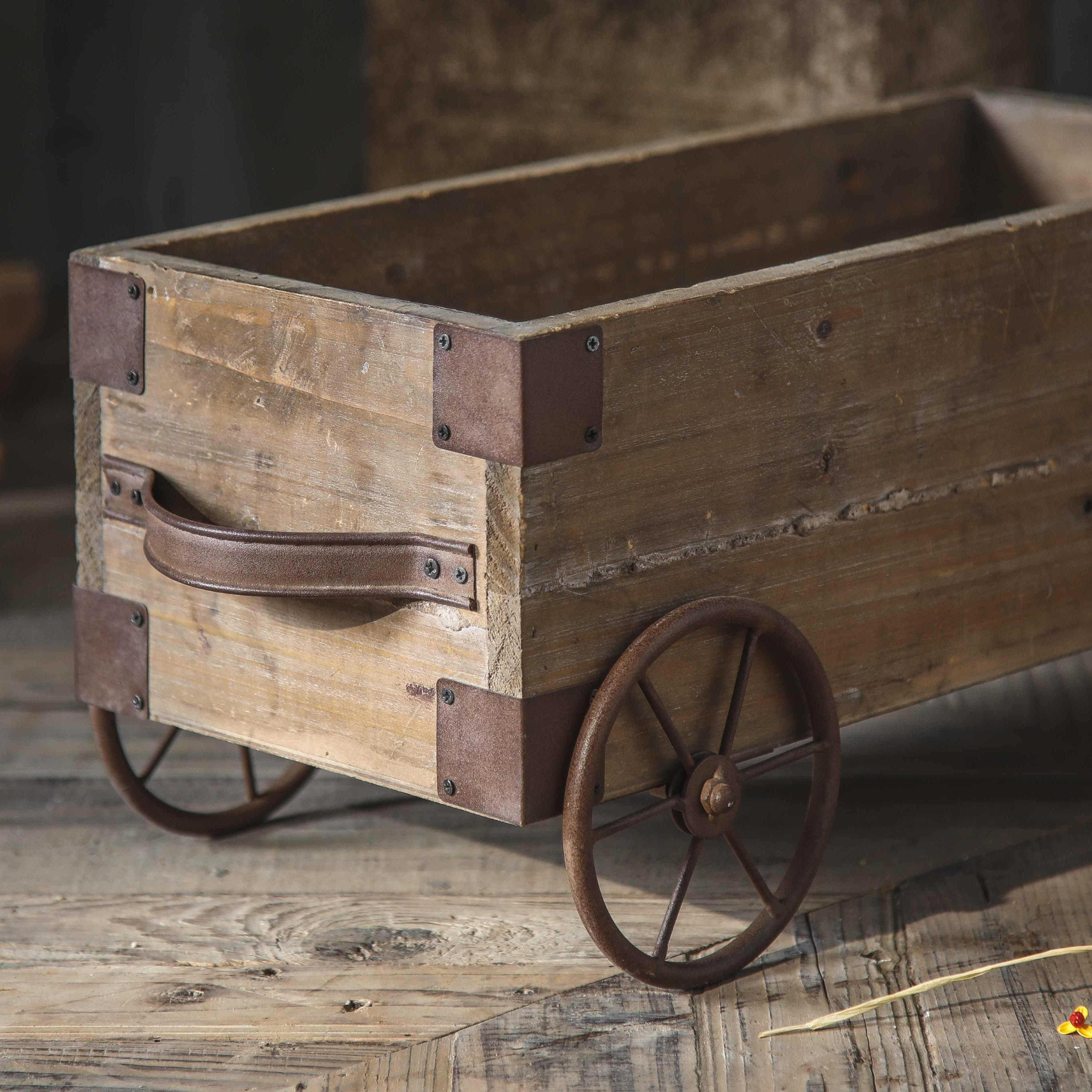 Empty wooden cart planter showing iron corner brackets, leather-style handles and spoked wheels