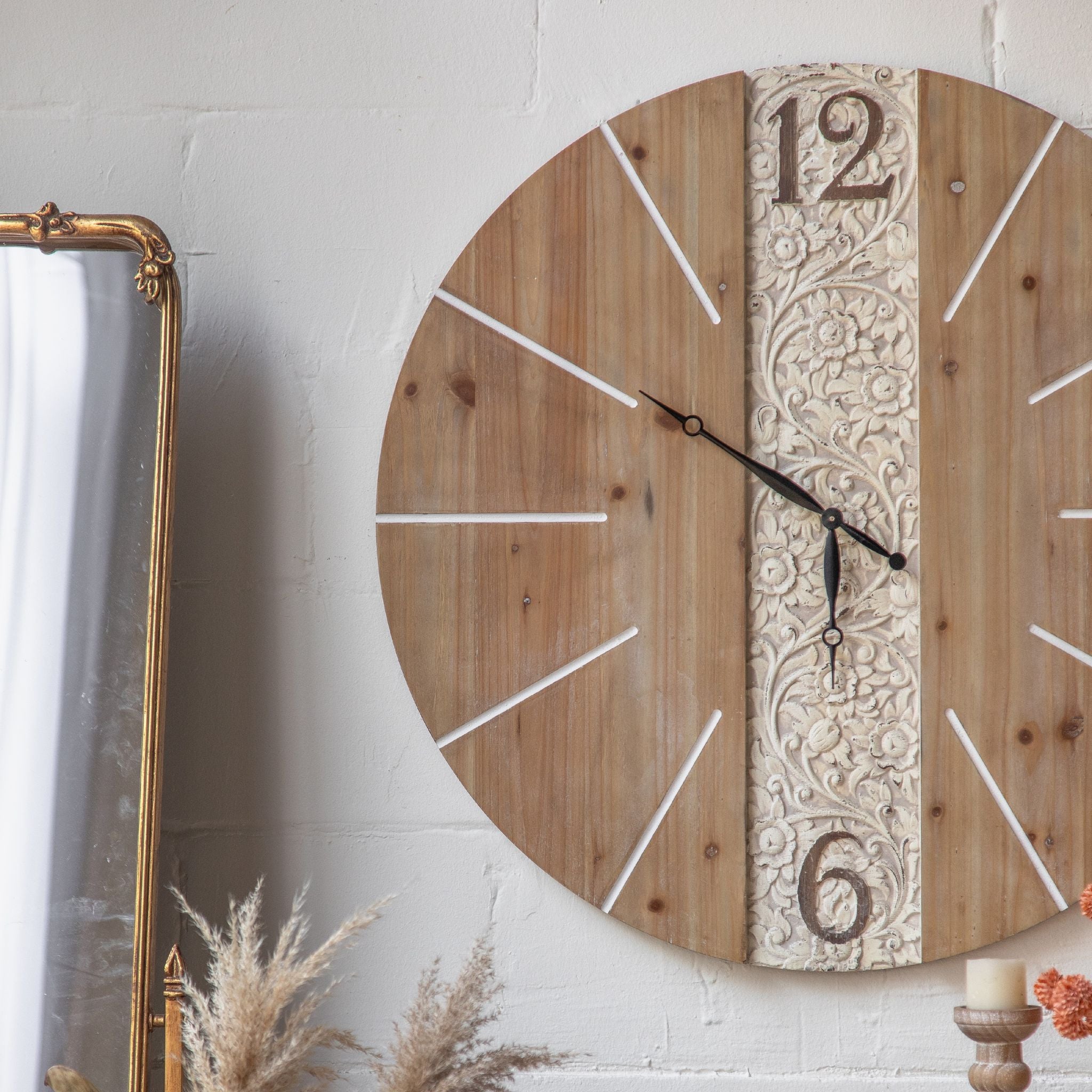 Three-quarter view of Pierre wall clock alongside a tall gilt-framed mirror, showing the proportions and the contrast between carved panel and plain wood sections