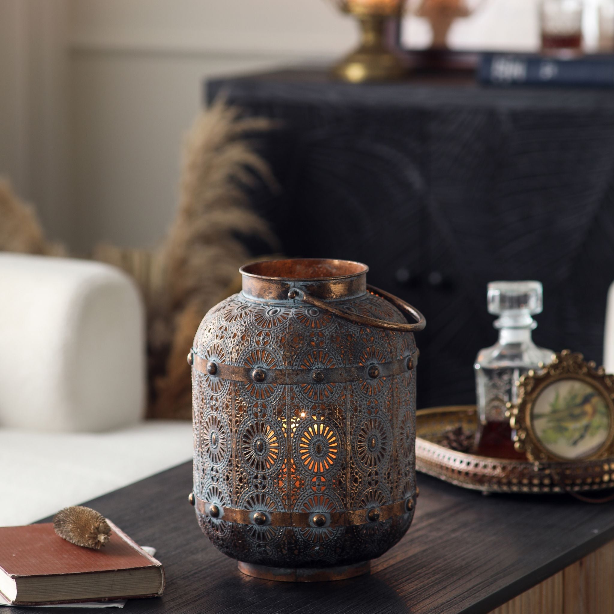 Rachelle pierced metal lantern lit on a dark table, styled with a tray and decanter.