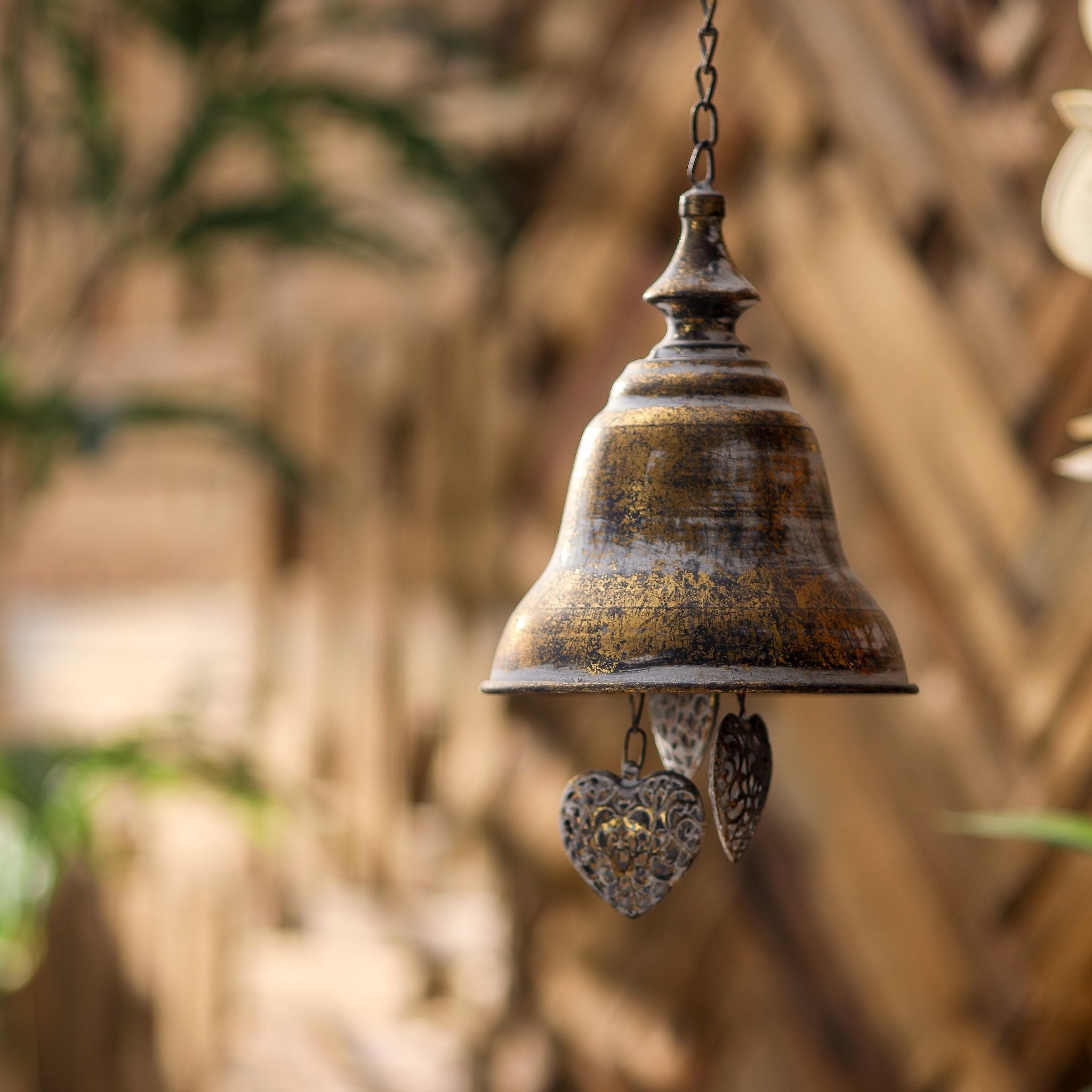 Rochelle antique gold hanging bell on a chain with filigree heart danglers, full view against a timber background.