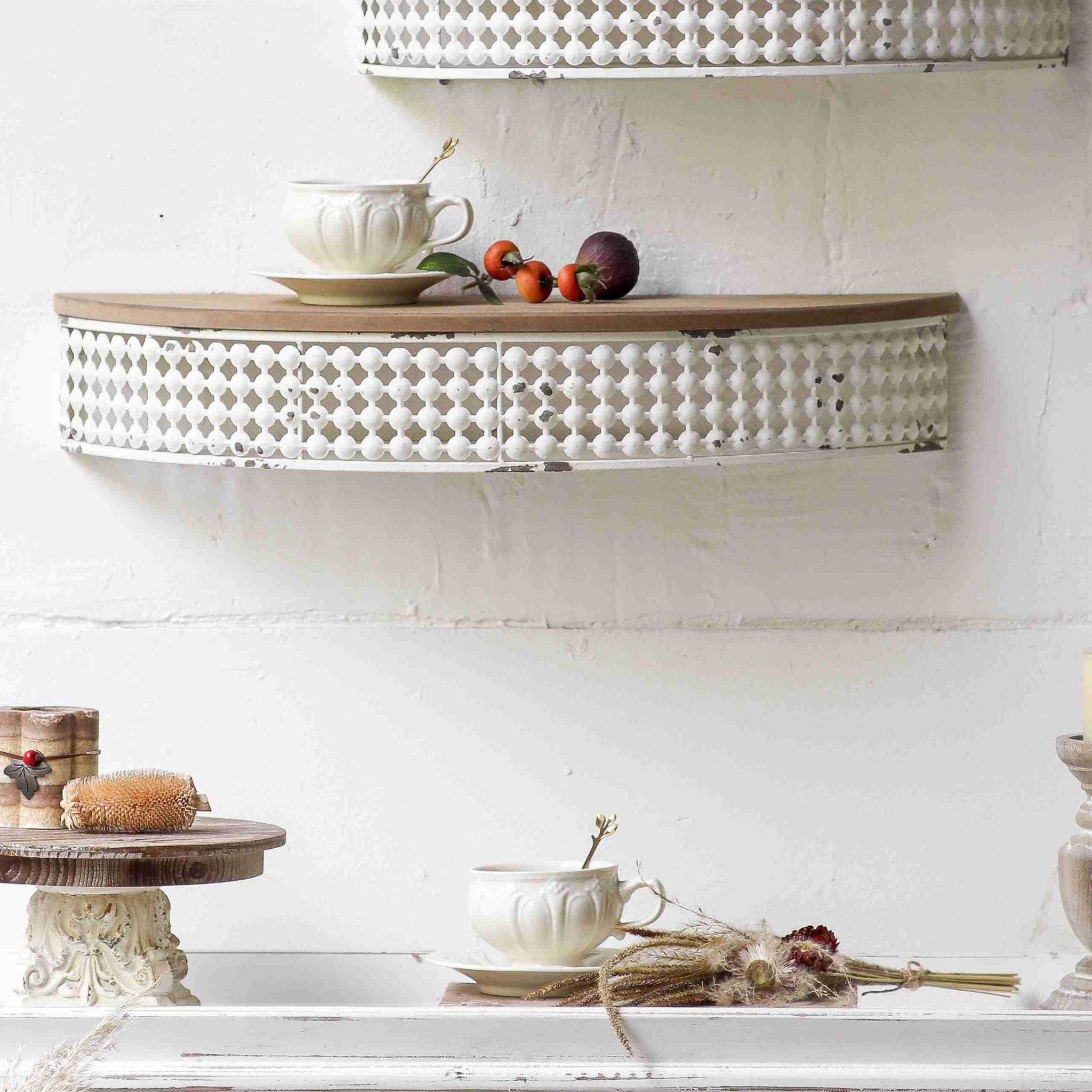 Rolande French Provincial half moon wall shelf mounted on a white wall, distressed white openwork metal gallery under a warm fir timber top, styled with a teacup and rosehips.