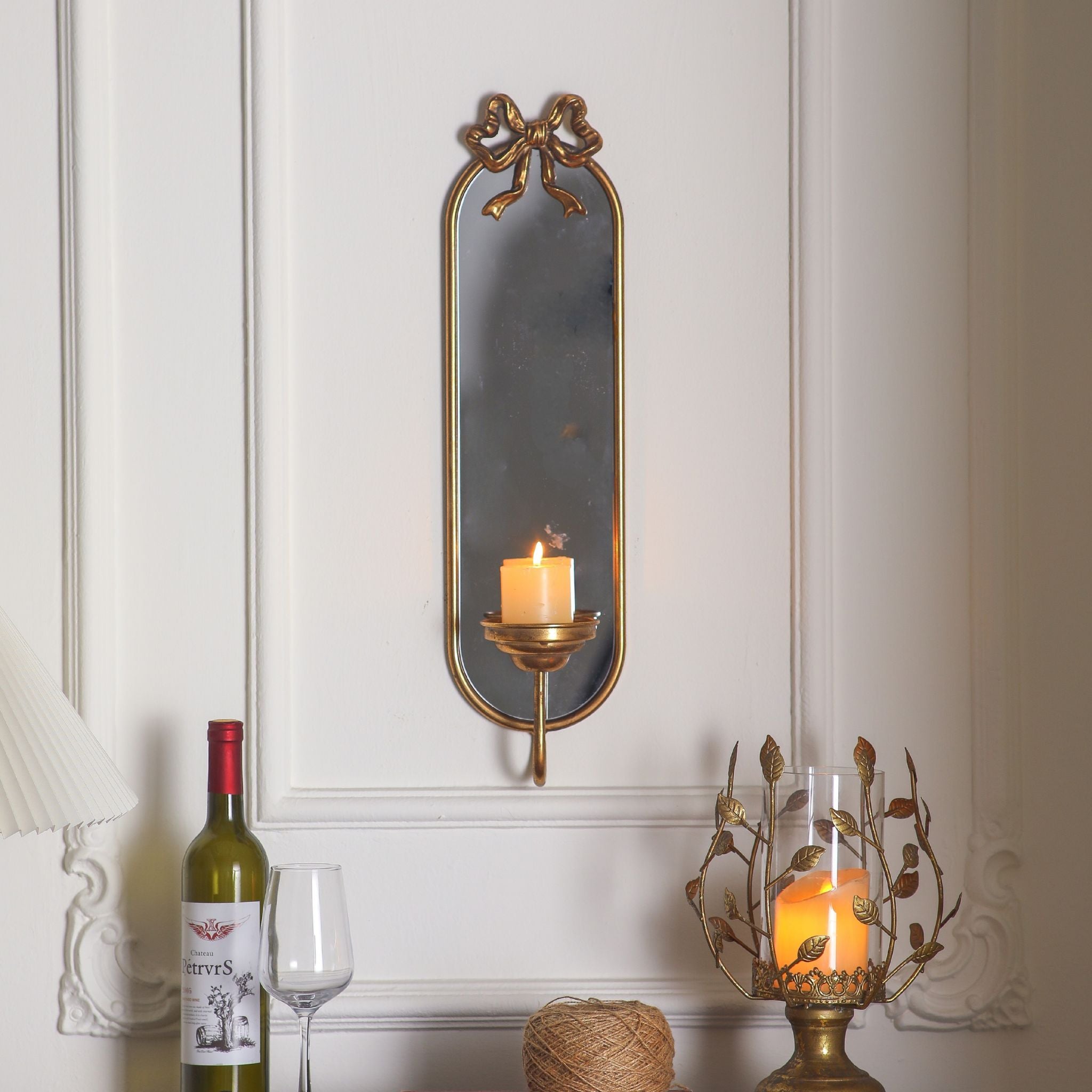 Aude mirror candle sconce lit with a pillar candle on a panelled wall