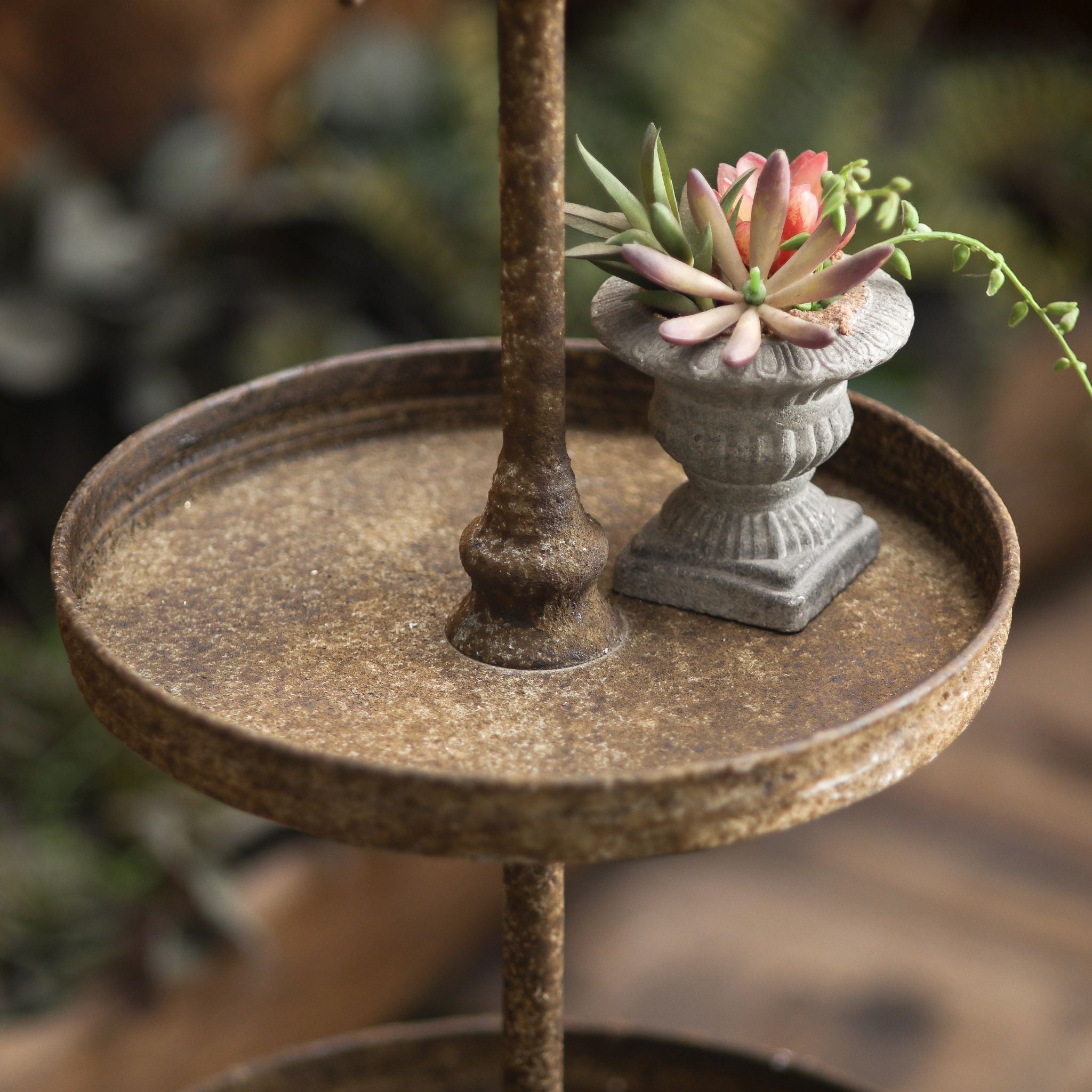 Detail of a Timéo tier, the rust-brown dish tray and turned centre pole, styled with a small stone urn and succulent.