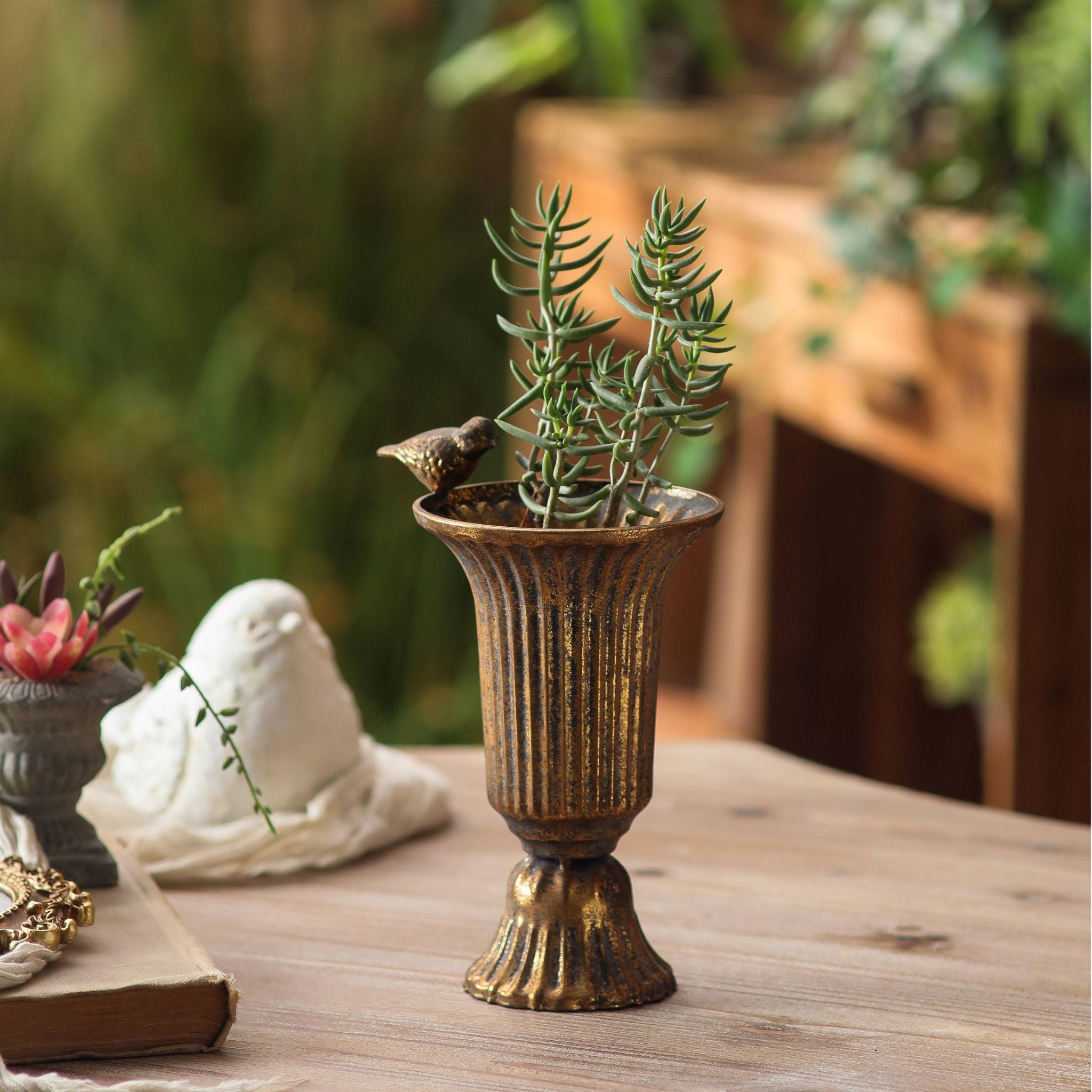 Valentine fluted urn vase with green succulent stems and the bird on the rim, on a garden table.