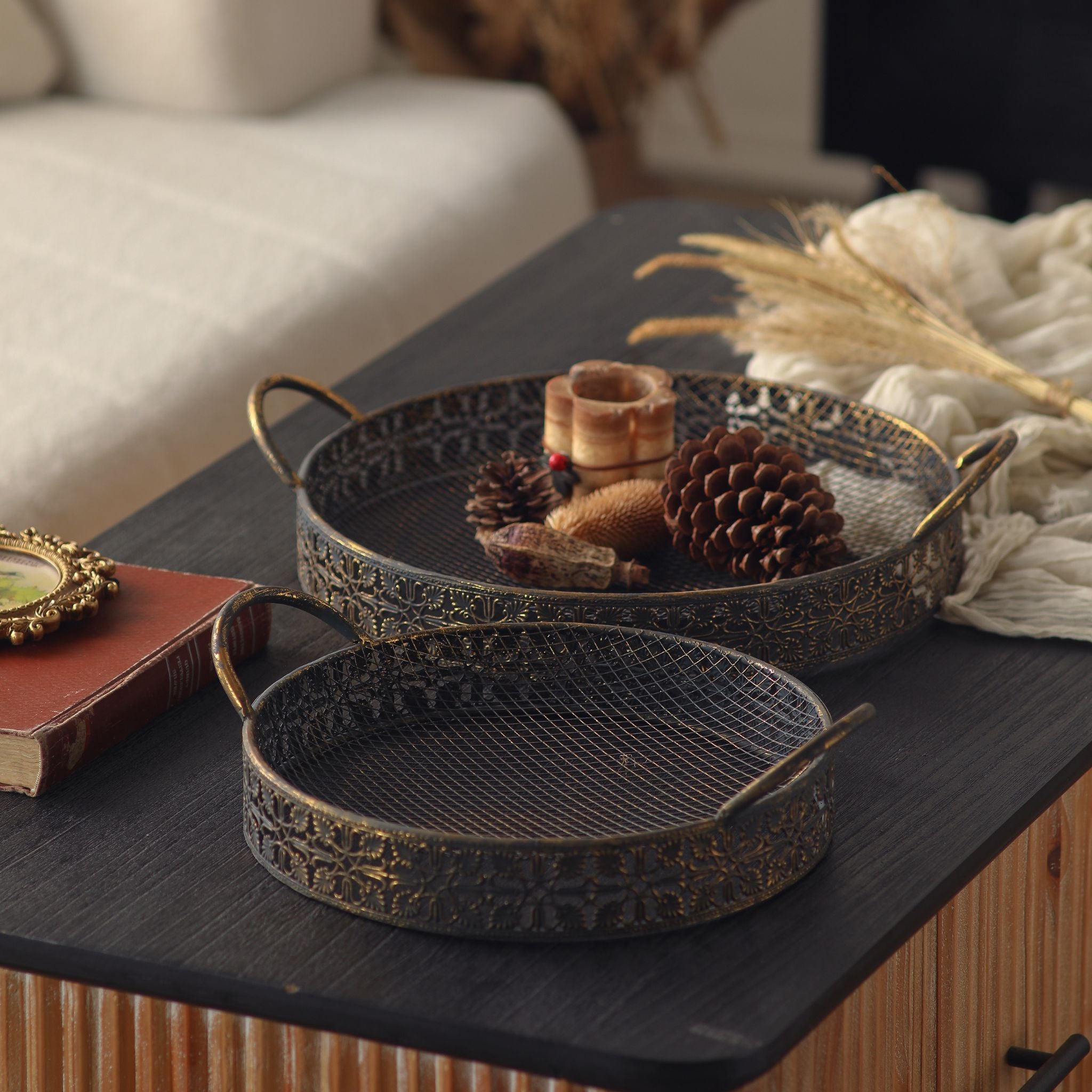 Valerie metal trays on a coffee table, the larger styled with pinecones and a candle holder, the smaller in front.