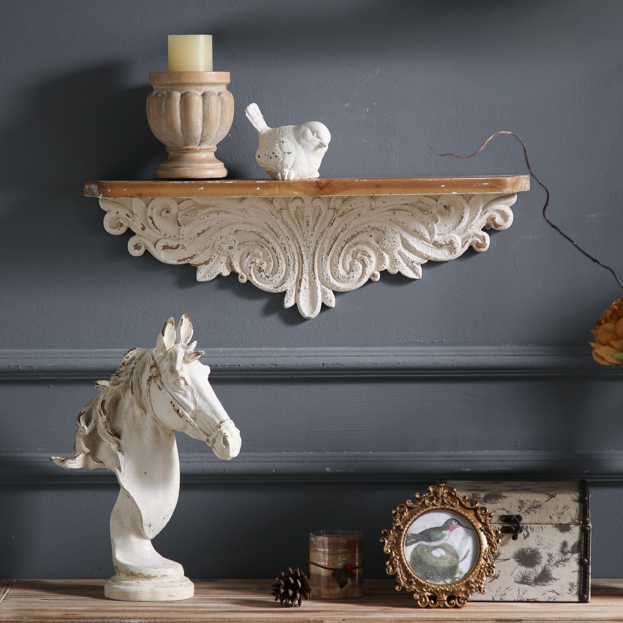 Vanessa French Provincial wall ledge shelf in distressed whitewash with carved acanthus scroll apron and warm timber top, styled with a fluted candle holder and small white bird on a charcoal wall. Hero