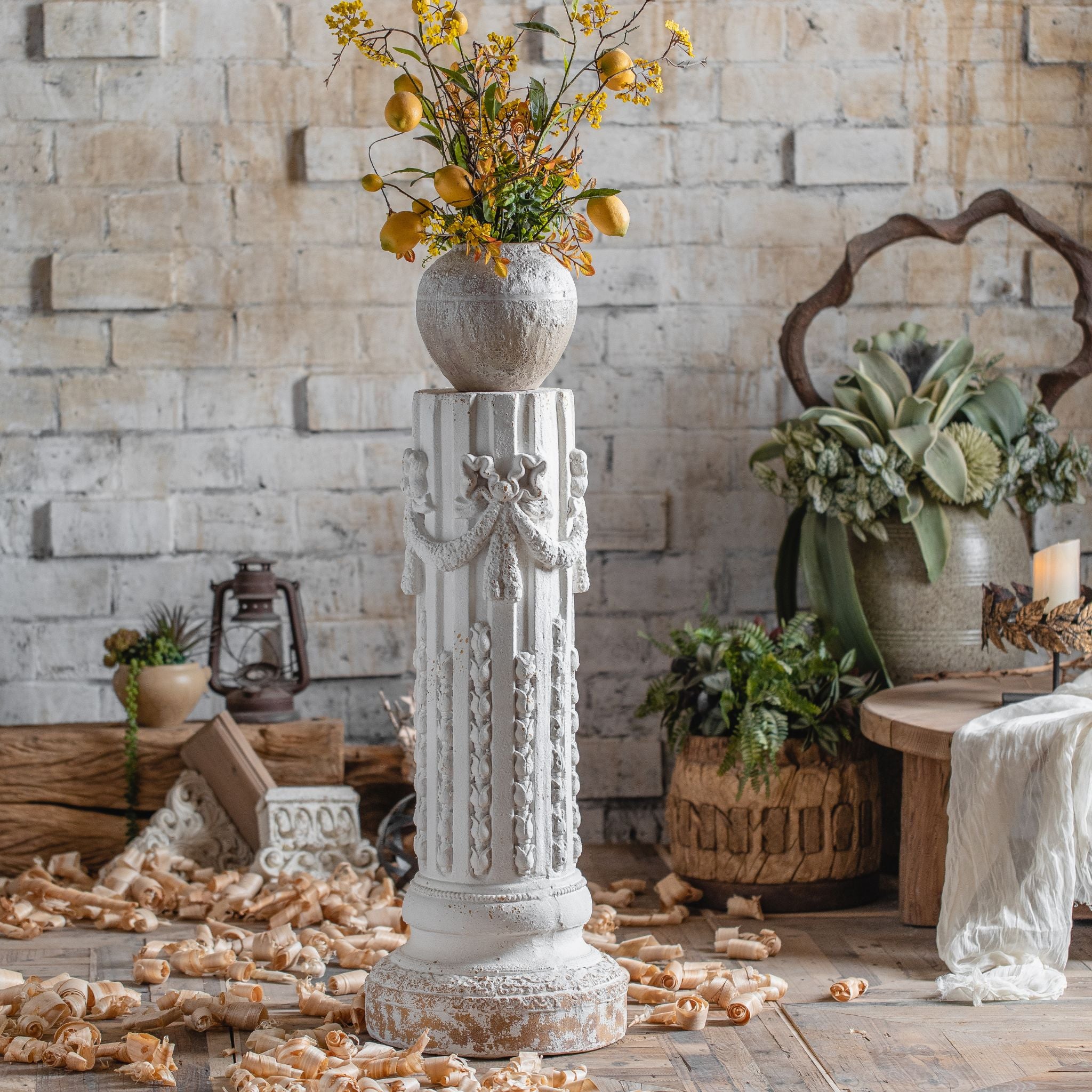 Close view of the carved ribbon and garland swags on the Bruna column pedestal in aged white