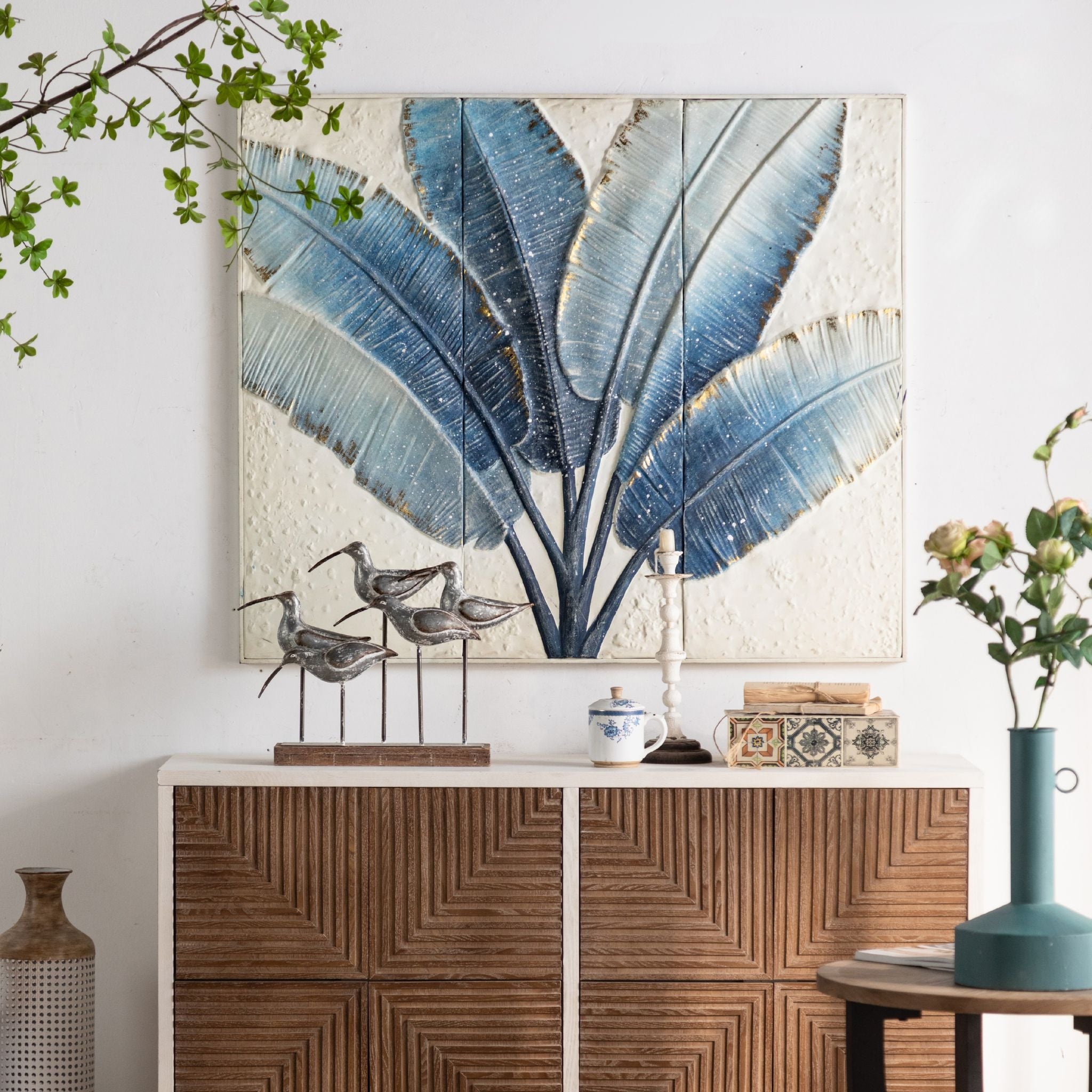 Tino embossed wall art with blue leaves and gold edges hung above a sideboard